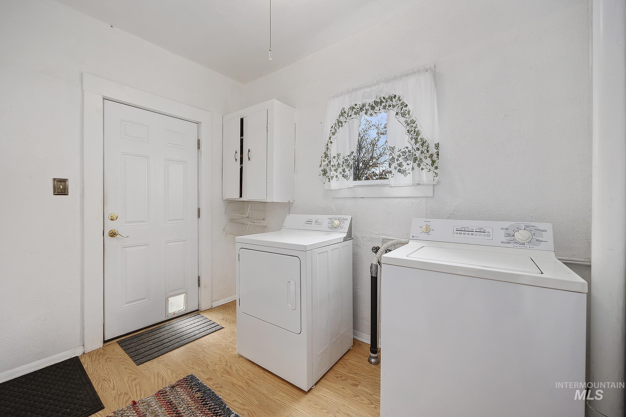 Laundry area with light wood-type flooring, washing machine and dryer, and a textured wall