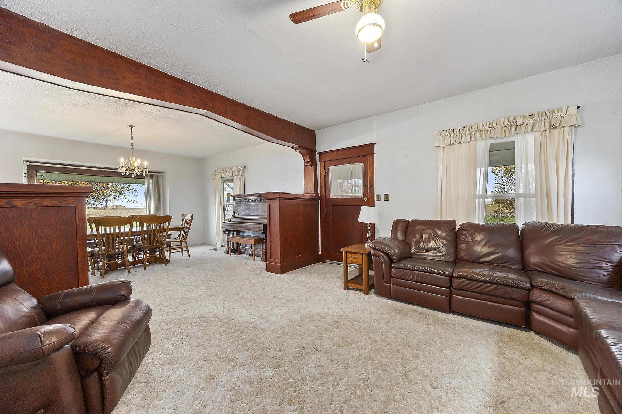 Living area featuring light colored carpet, beamed ceiling, ceiling fan, and a chandelier