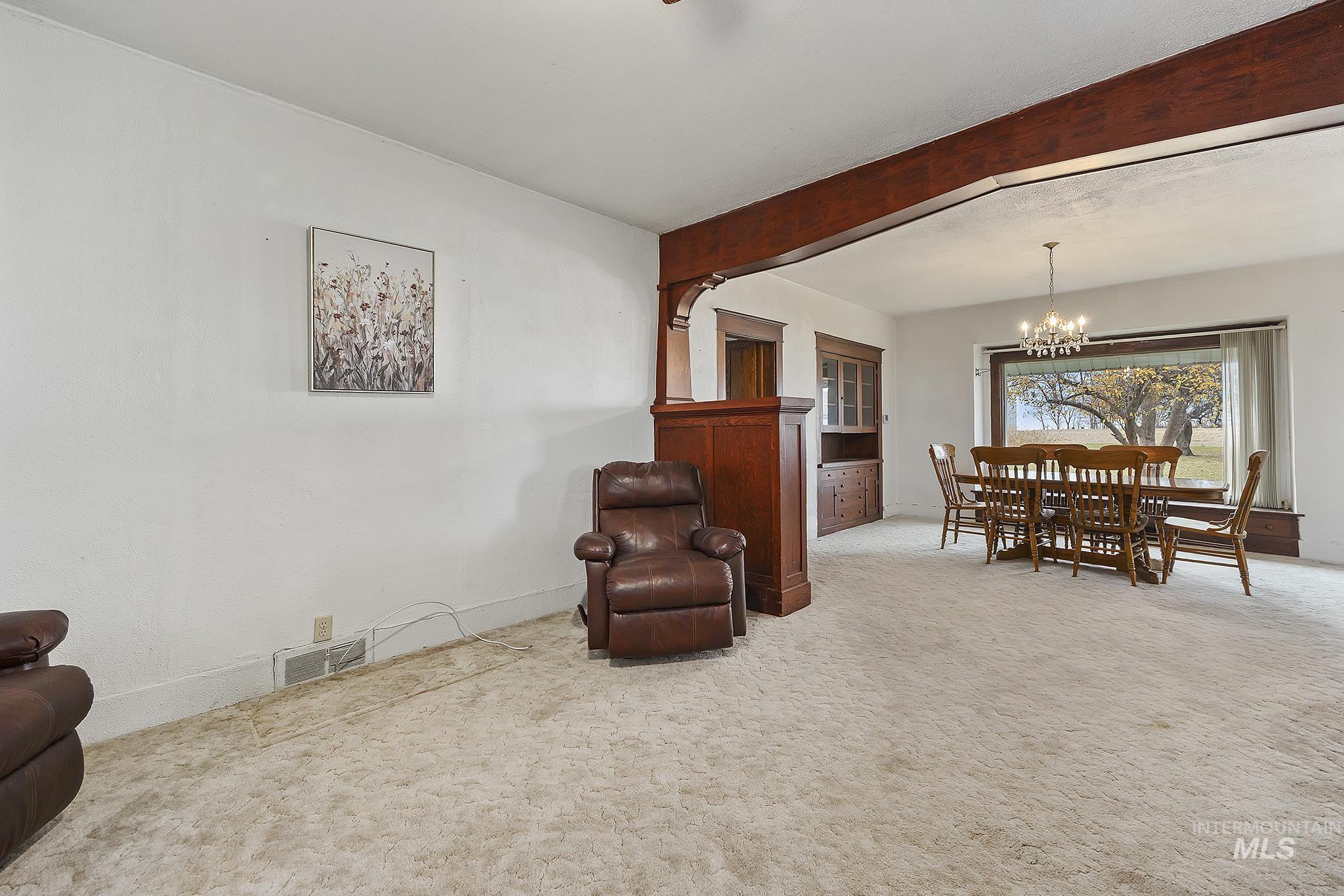 Living area with carpet flooring, beamed ceiling, and a chandelier