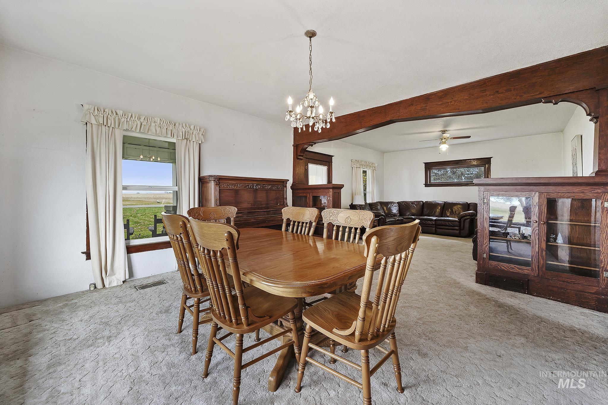 Dining room featuring light carpet, beamed ceiling, a chandelier, and a ceiling fan