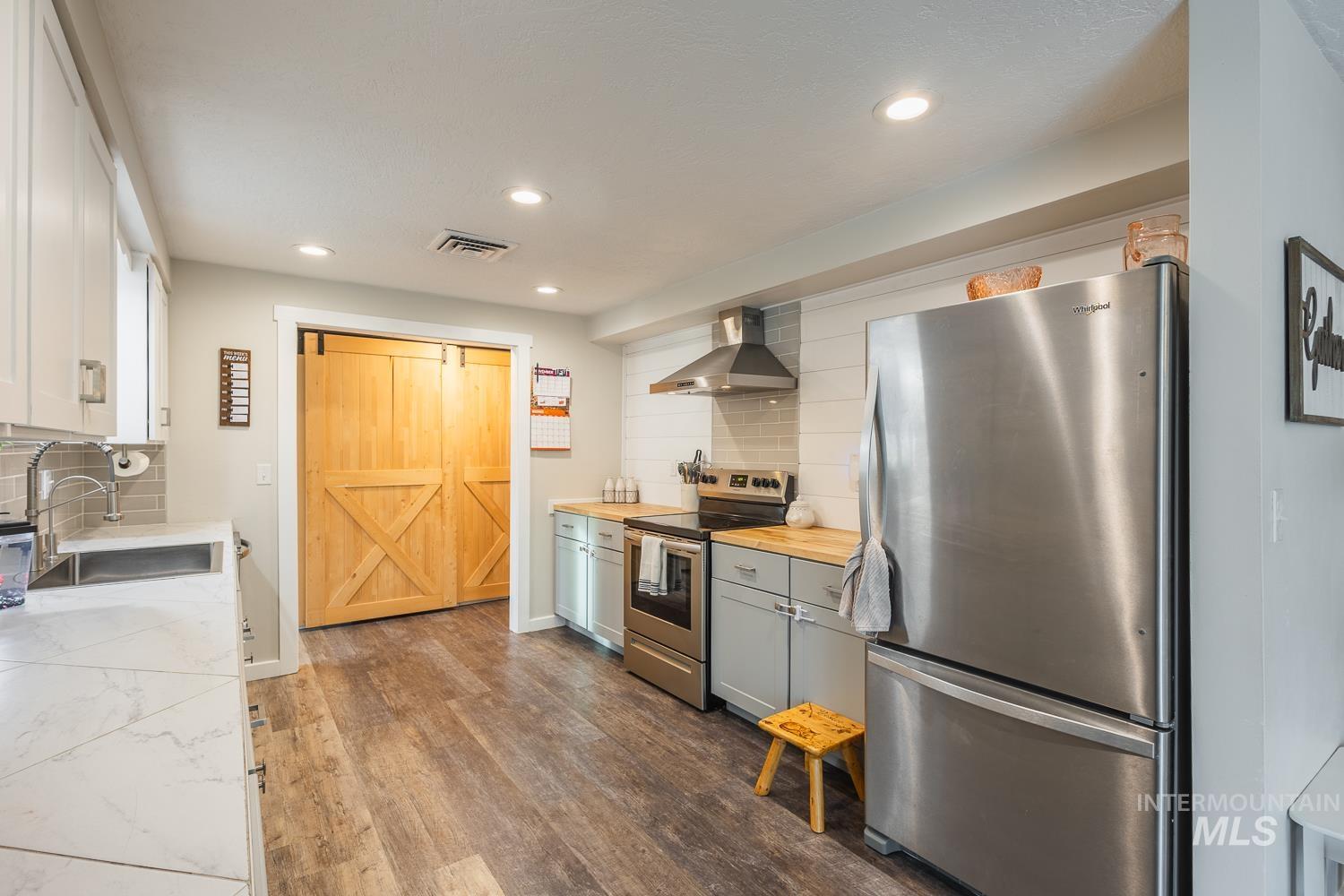 Kitchen with tasteful backsplash, stainless steel appliances, dark wood-style flooring, wall chimney range hood, and recessed lighting