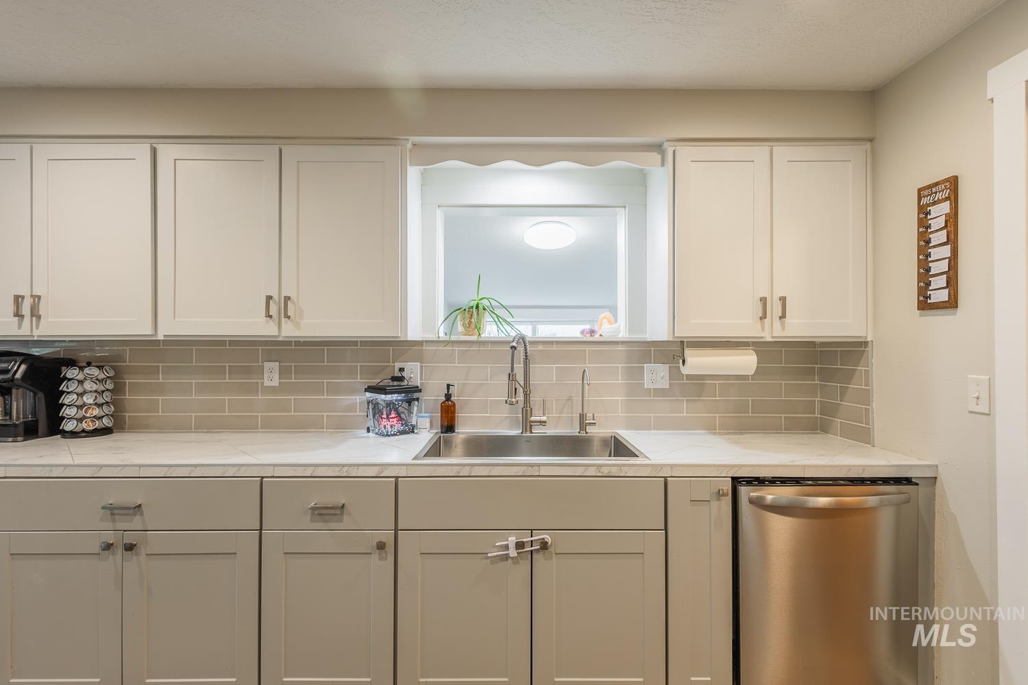 Kitchen featuring stainless steel dishwasher, decorative backsplash, white cabinets, and a textured ceiling