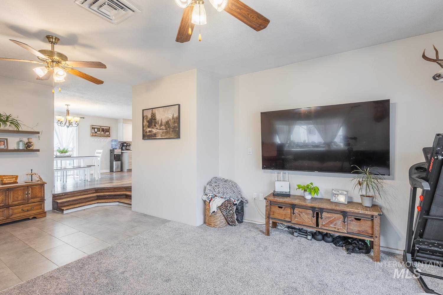 Tiled living room featuring a ceiling fan, carpet floors, and a chandelier