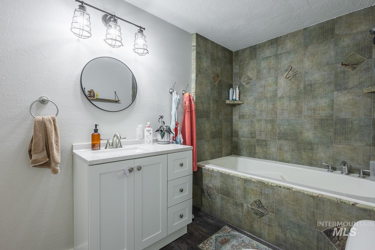 Full bathroom featuring vanity, tiled shower / bath, a textured wall, a textured ceiling, and dark wood finished floors