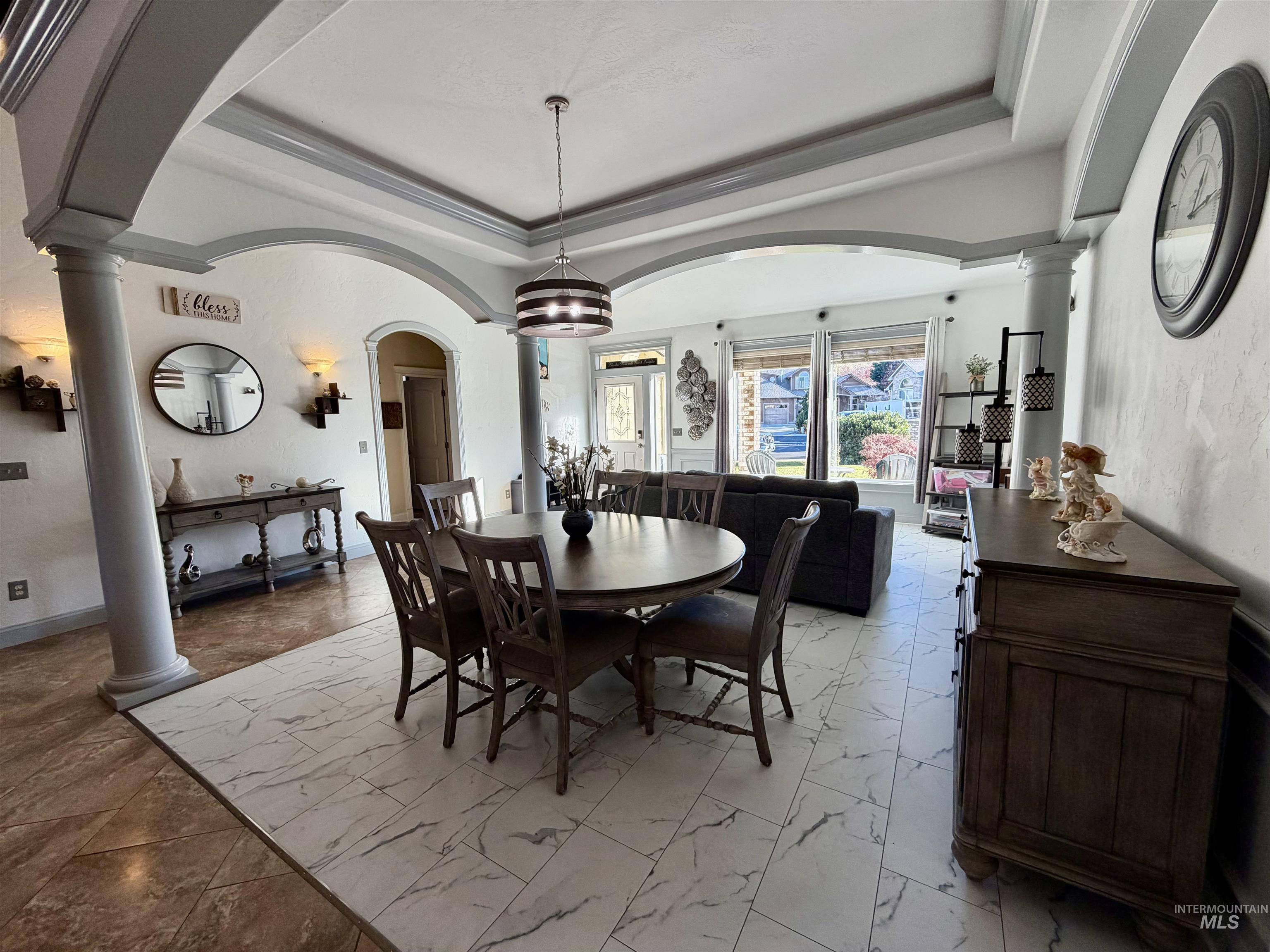 Dining space featuring decorative columns, arched walkways, a tray ceiling, and ornamental molding