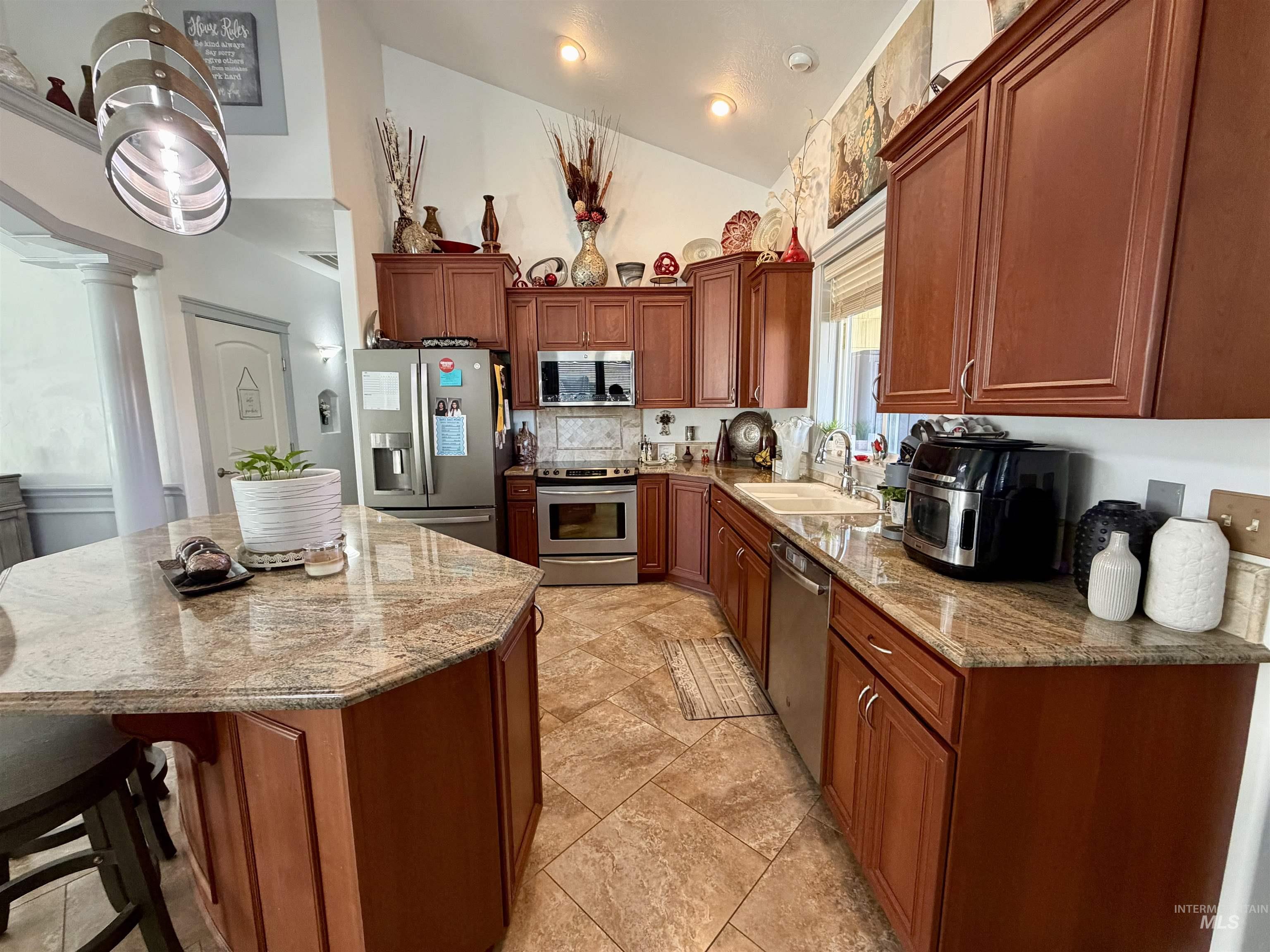 Kitchen with light stone countertops, stainless steel appliances, a kitchen breakfast bar, brown cabinetry, and a center island