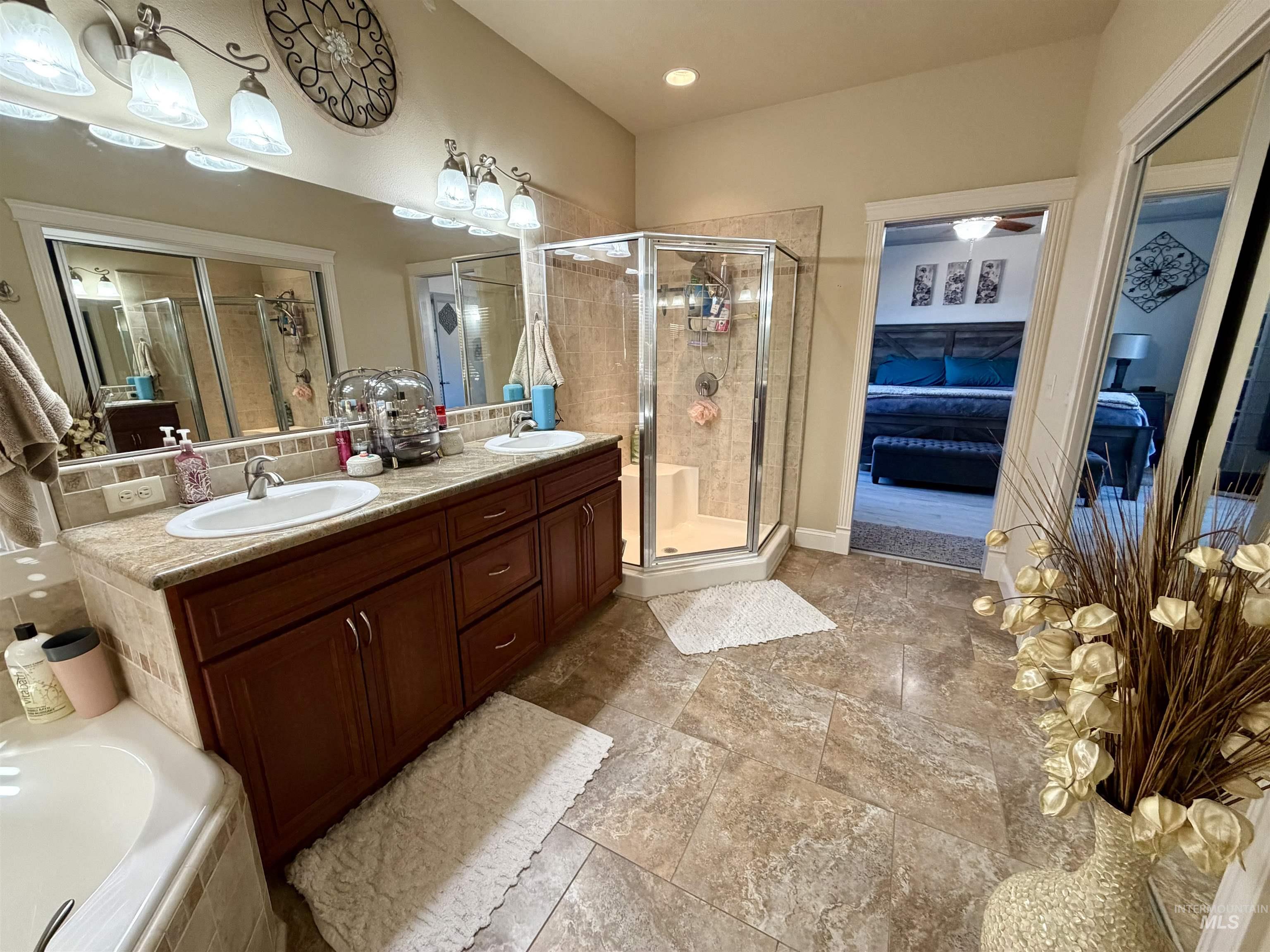 Ensuite bathroom with double vanity, a relaxing tiled tub, a stall shower, and decorative backsplash