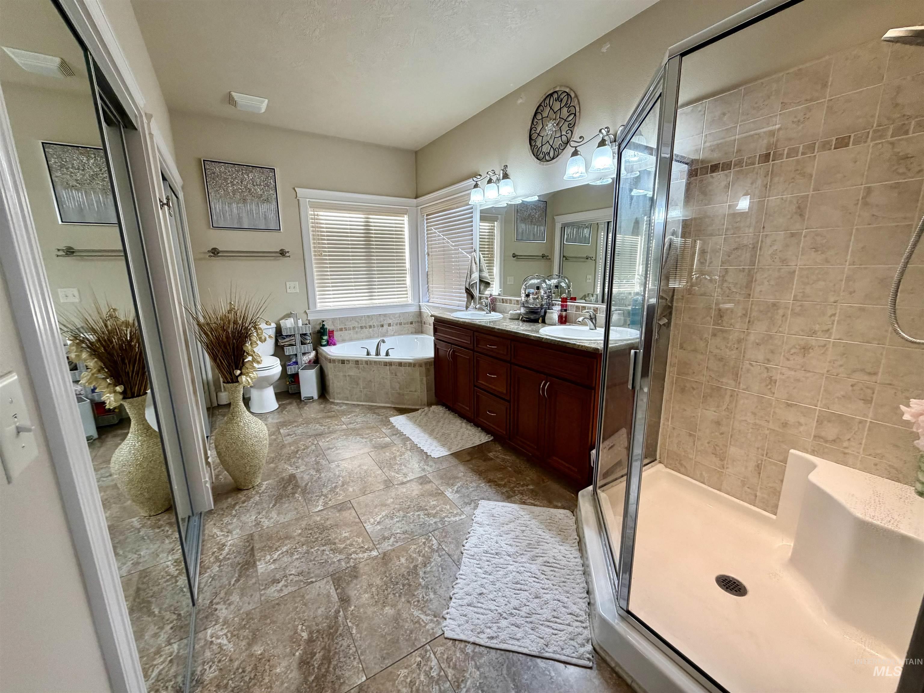 Full bath with a shower stall, double vanity, a garden tub, and dark stone finish flooring