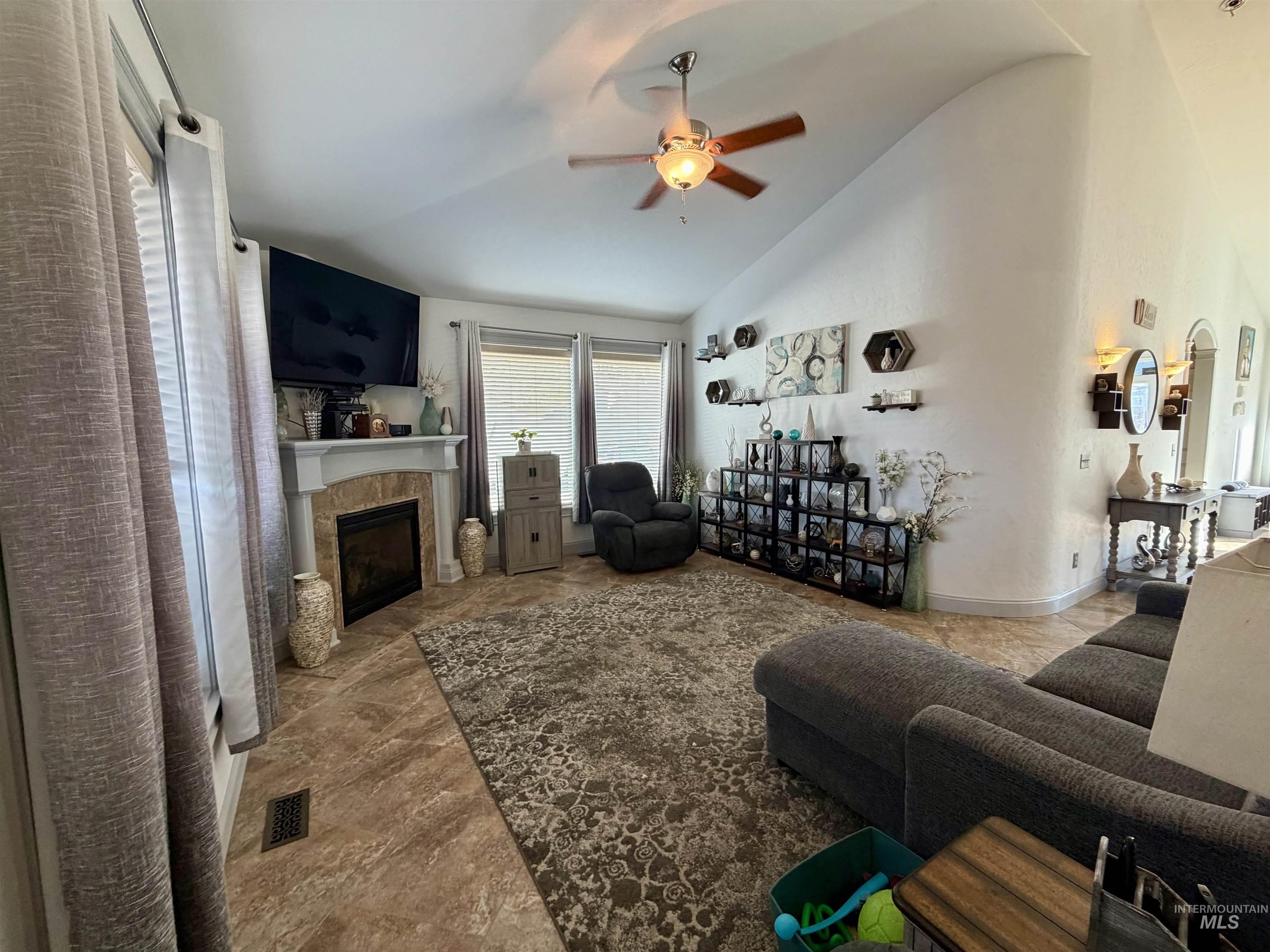 Living area with a tiled fireplace, ceiling fan, and high vaulted ceiling