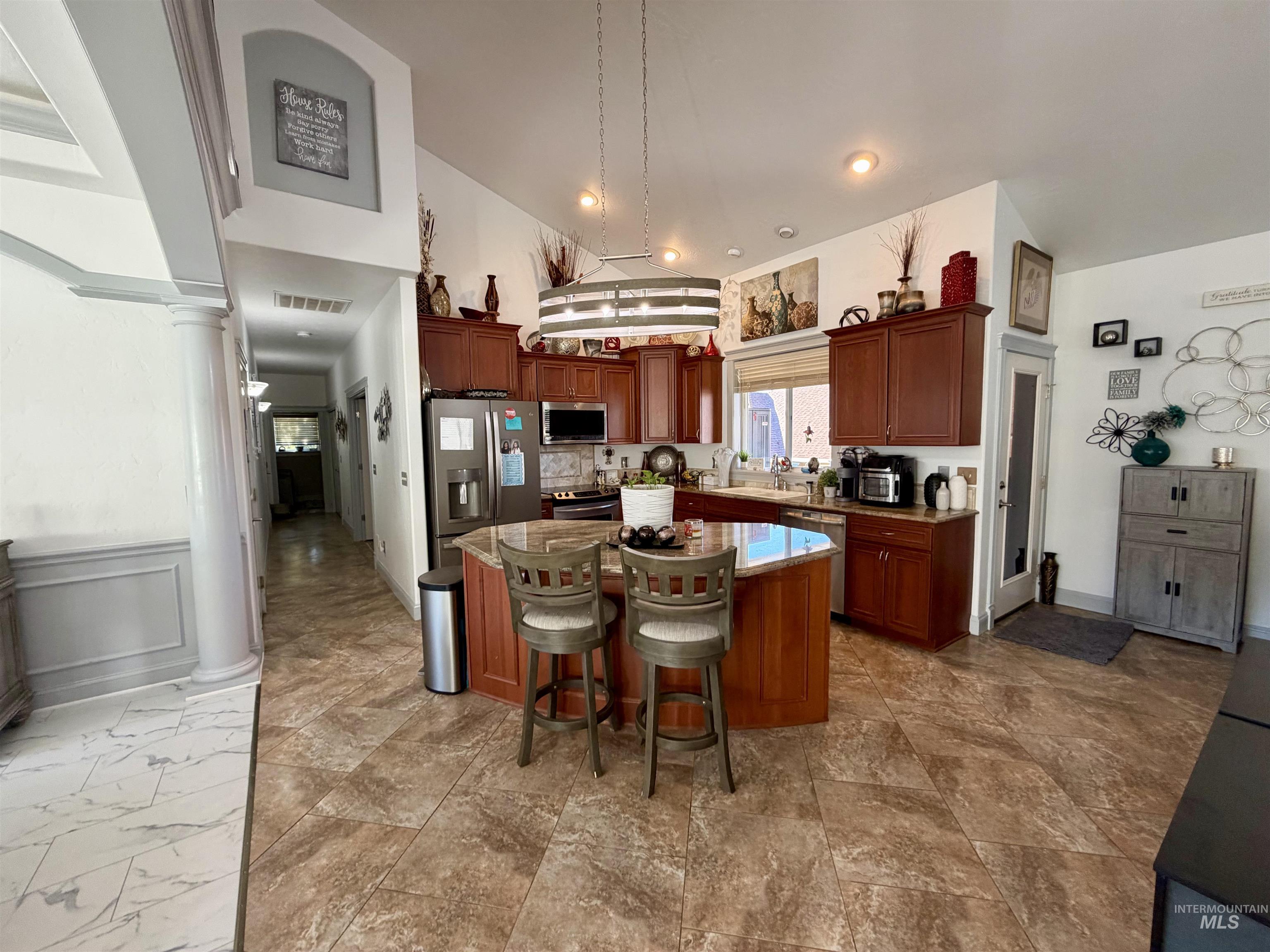 Kitchen featuring a center island, decorative columns, a kitchen bar, appliances with stainless steel finishes, and hanging light fixtures