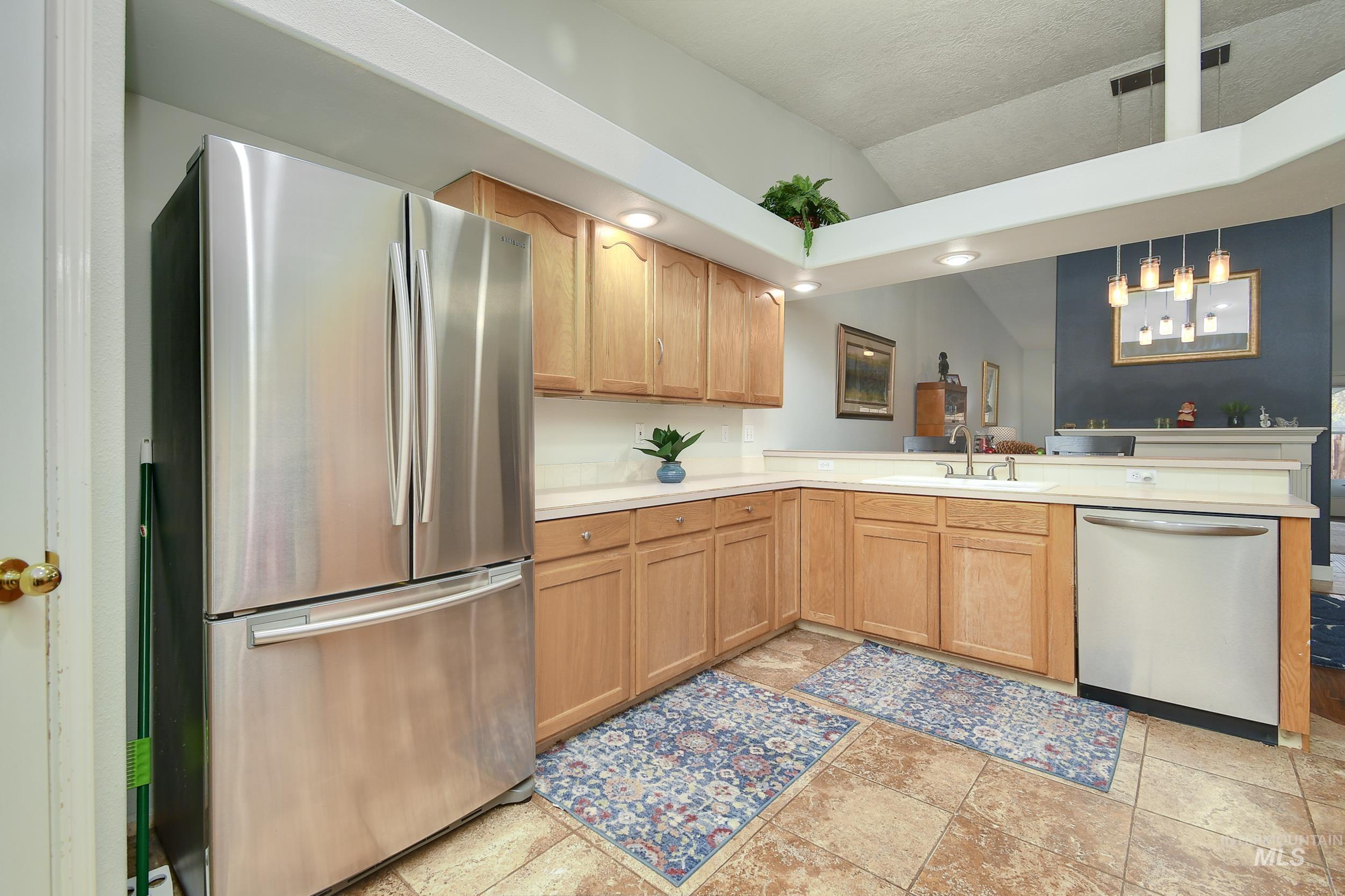 Kitchen featuring appliances with stainless steel finishes, light countertops, decorative light fixtures, a peninsula, and light brown cabinetry