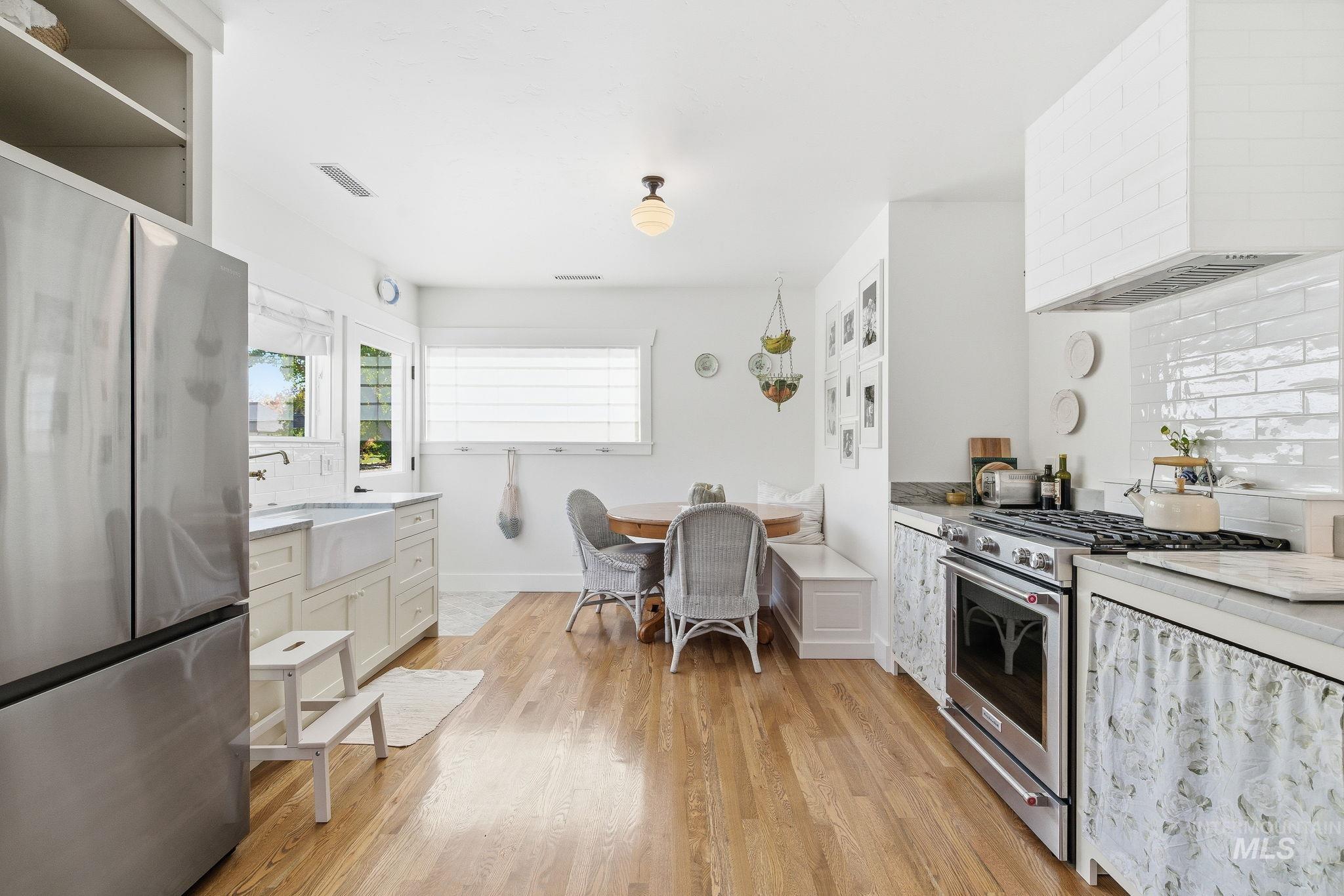 Kitchen featuring tasteful backsplash, appliances with stainless steel finishes, wall chimney range hood, light wood-style flooring, and white cabinets