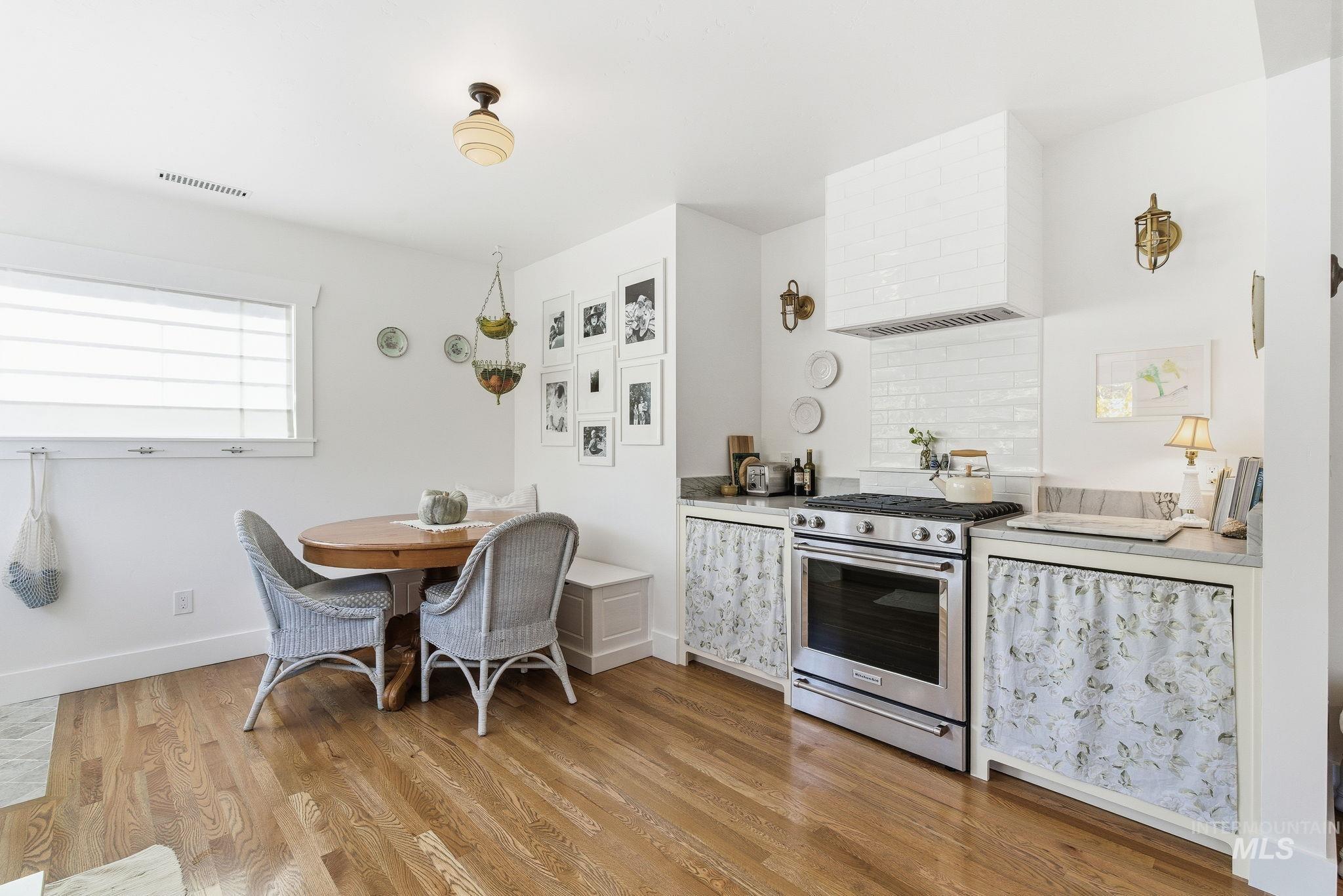 Kitchen featuring gas range, wall chimney exhaust hood, light wood finished floors, light countertops, and tasteful backsplash