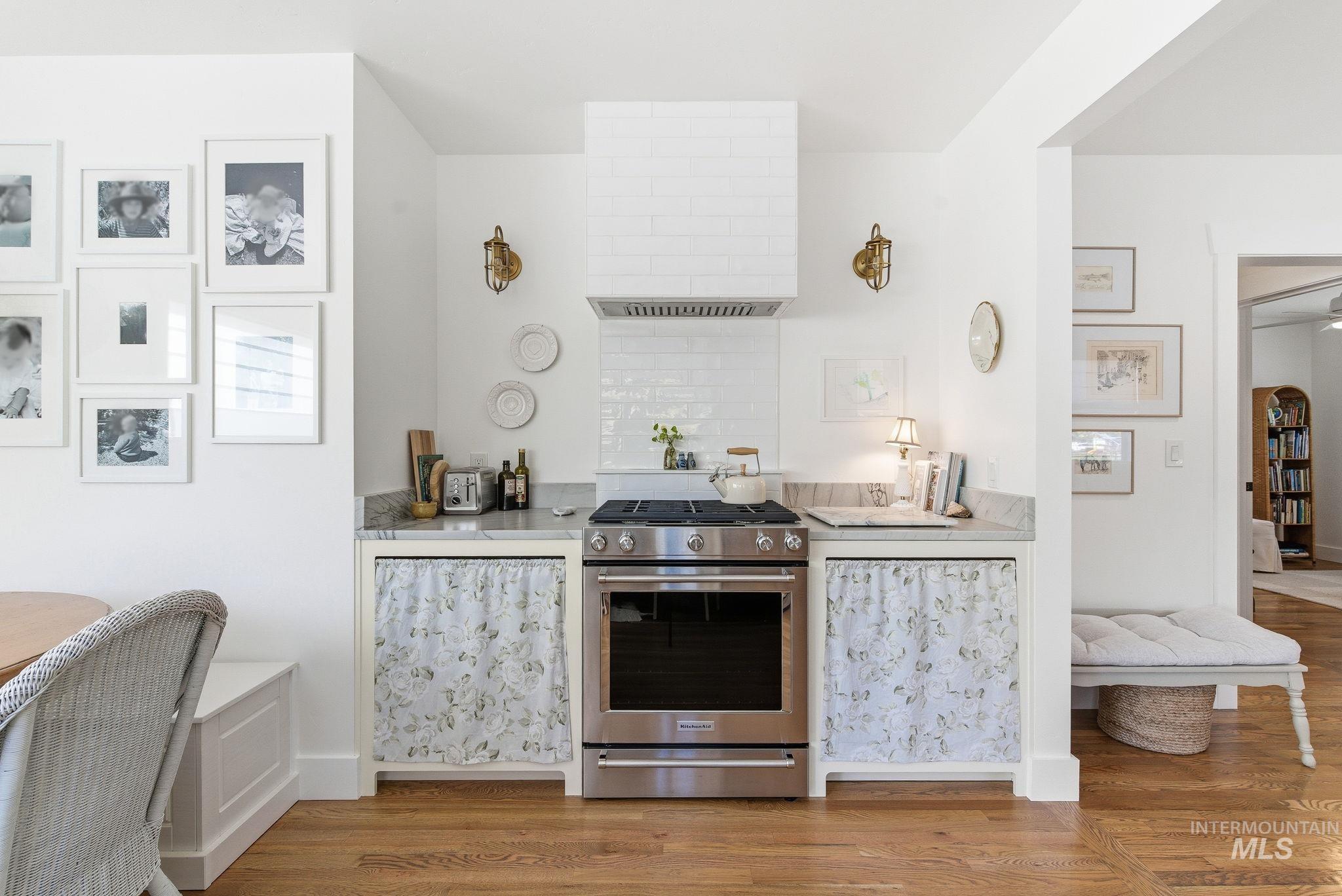 Kitchen with stainless steel gas stove, extractor fan, light wood-style floors, light stone counters, and white cabinets