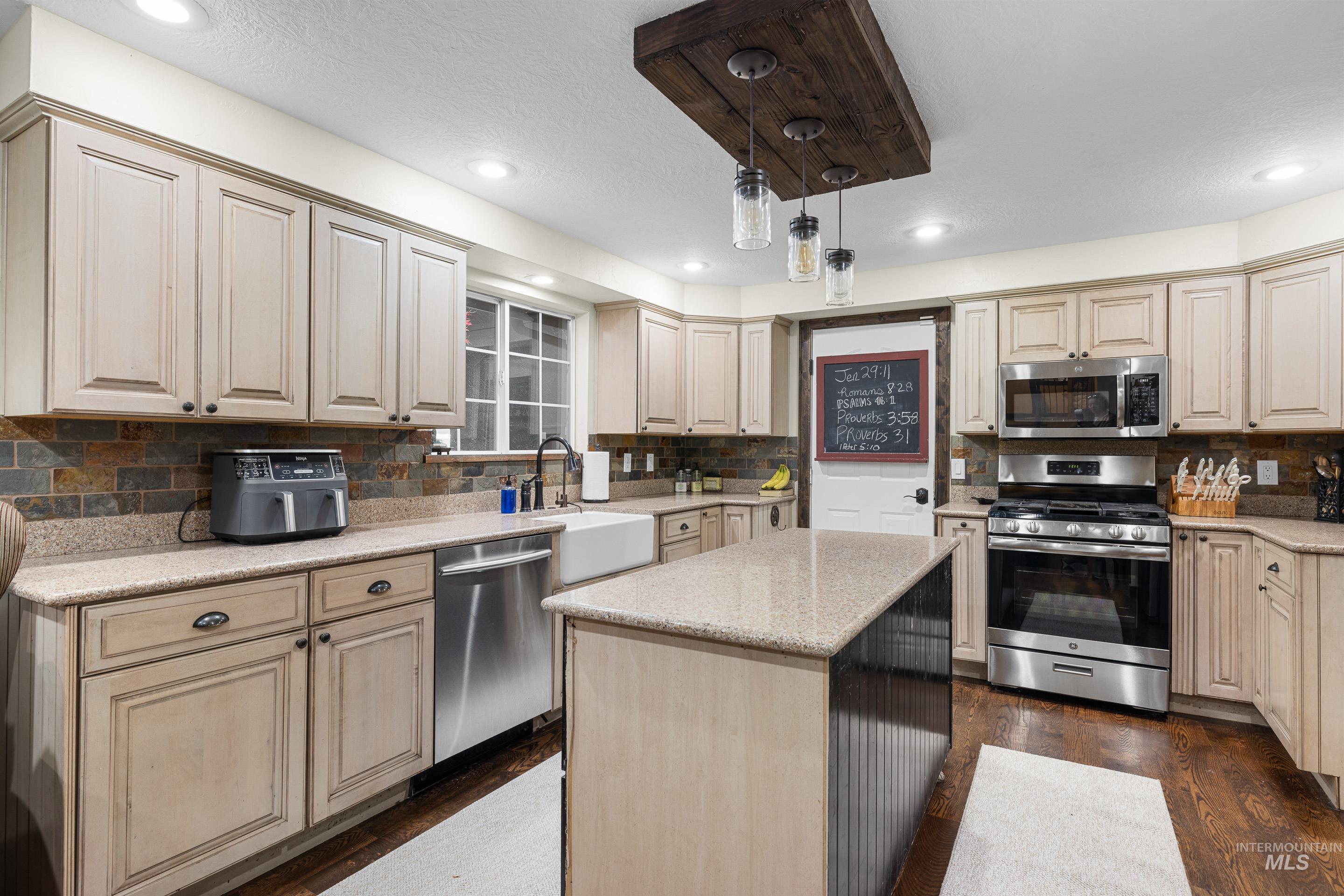 Kitchen featuring appliances with stainless steel finishes, light stone countertops, a kitchen island, pendant lighting, and dark wood-style flooring