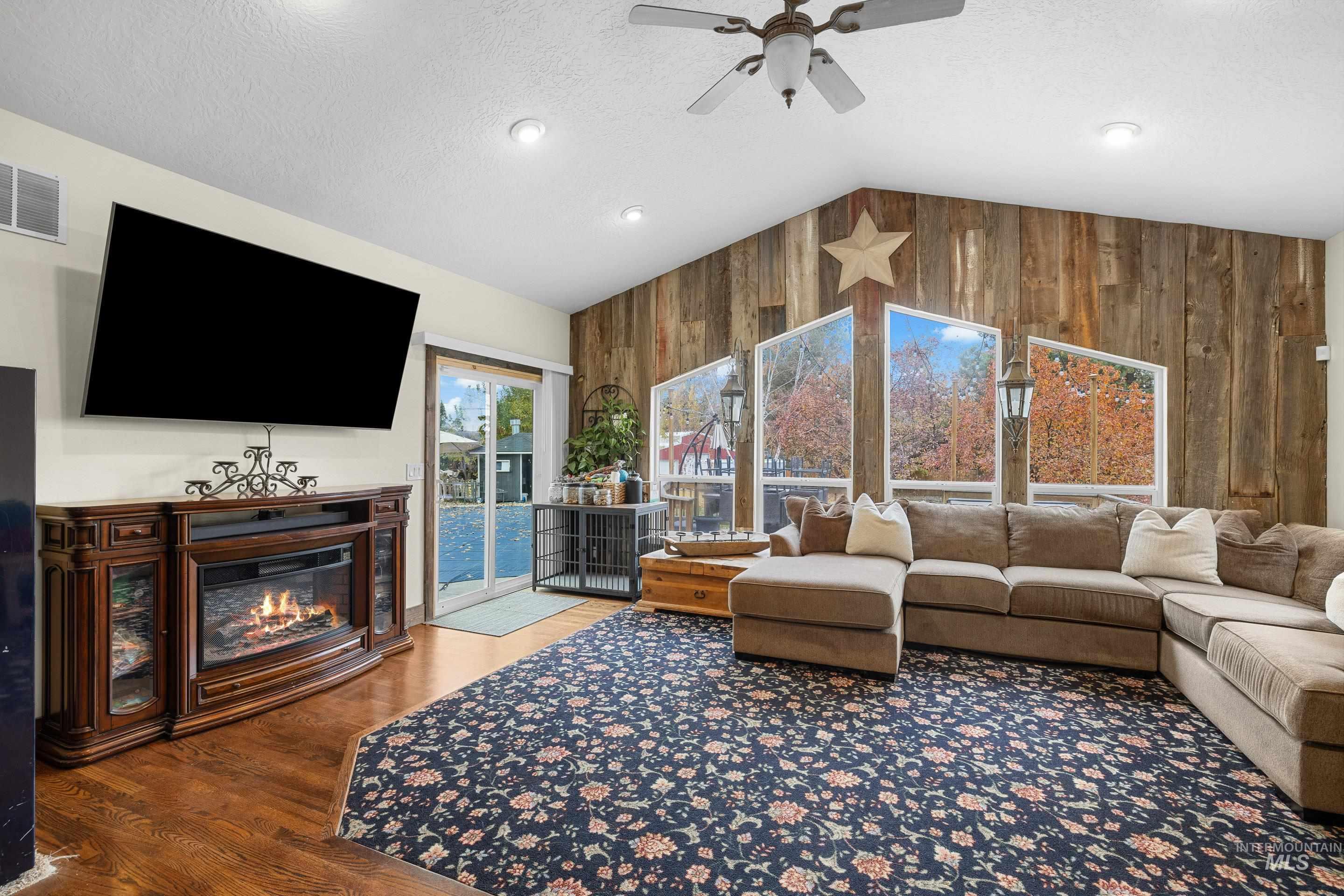 Living room with wooden walls, lofted ceiling, a glass covered fireplace, a textured ceiling, and wood finished floors