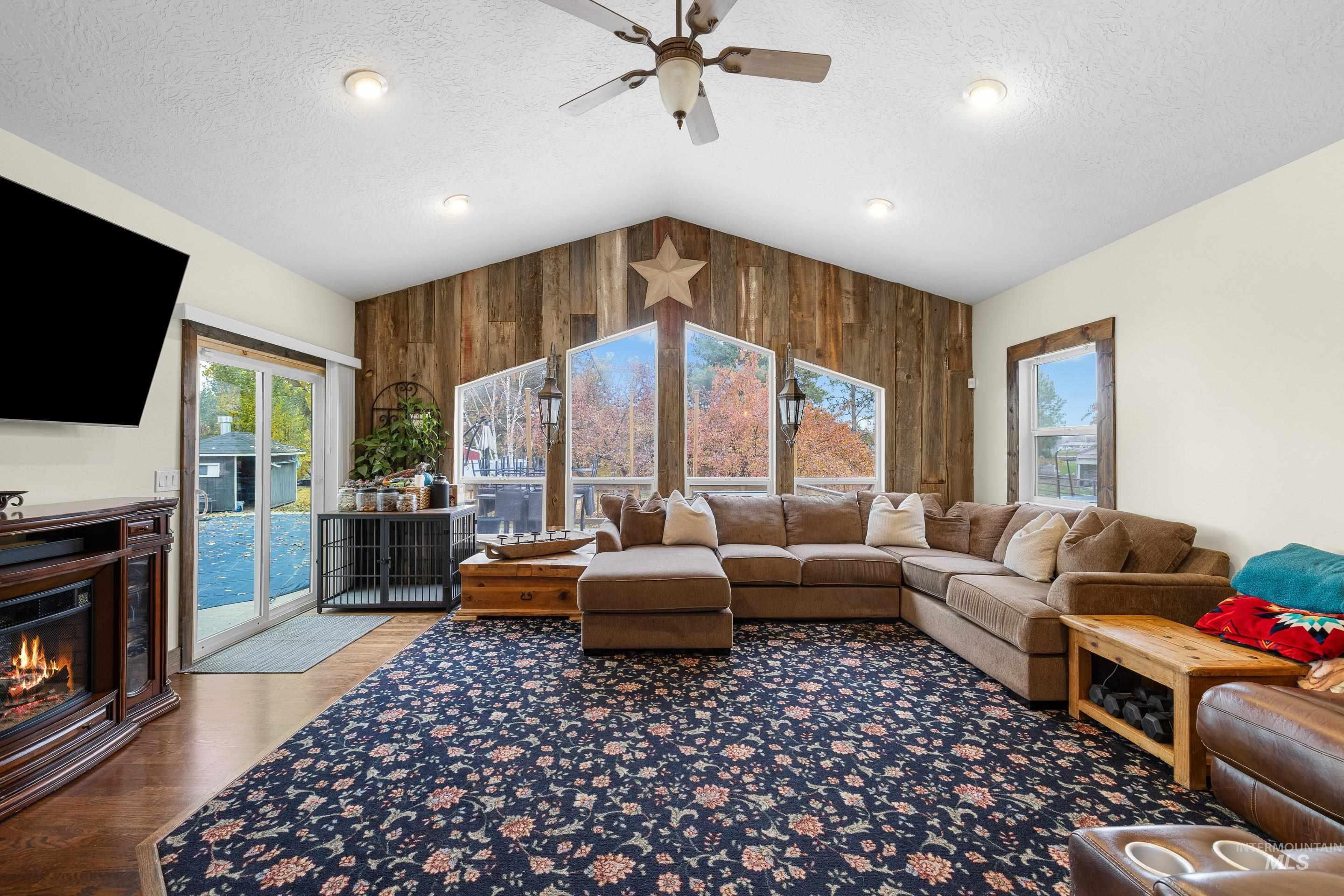 Living room featuring a glass covered fireplace, wood walls, wood finished floors, lofted ceiling, and a textured ceiling
