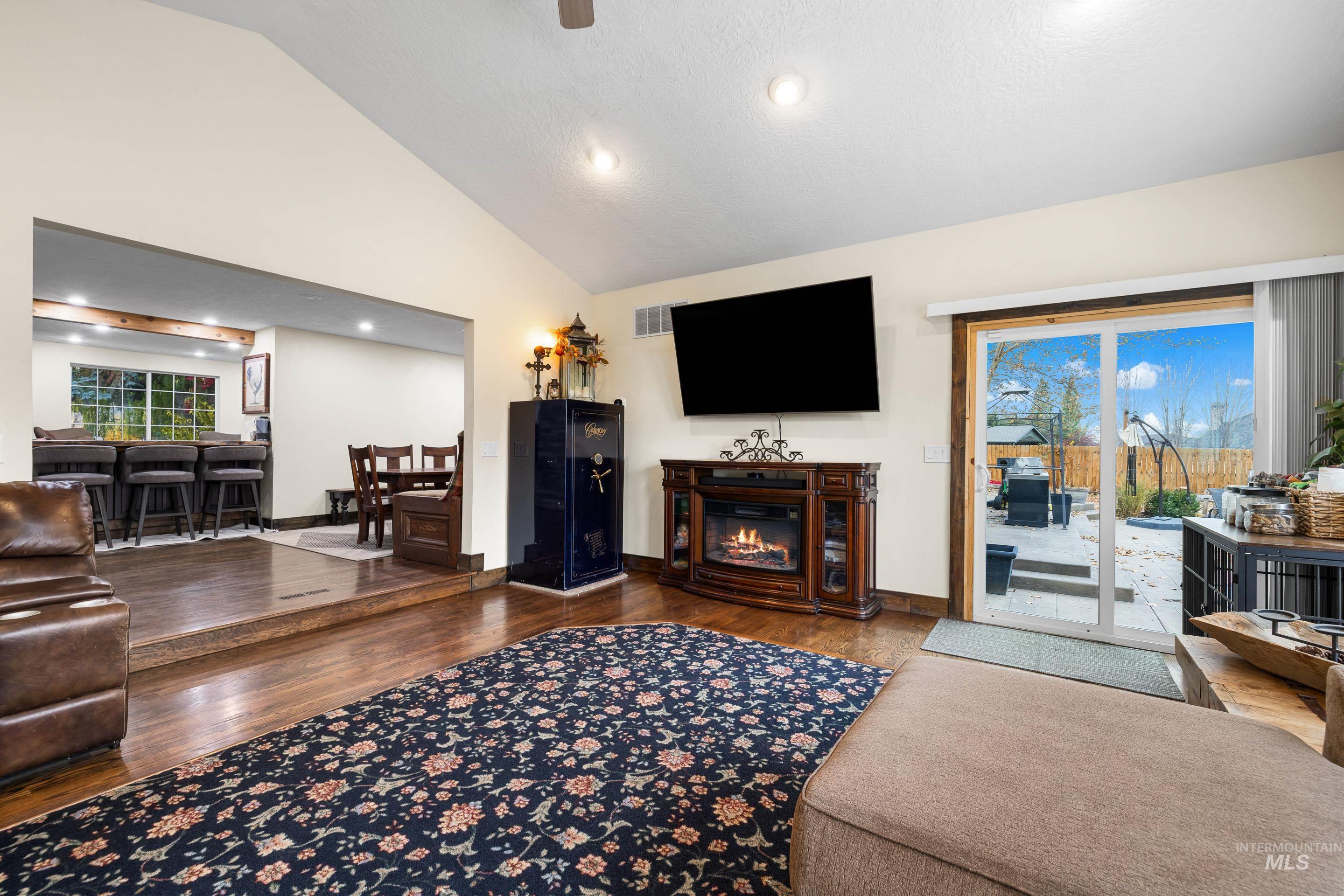 Living room with dark wood-style flooring, a glass covered fireplace, recessed lighting, and high vaulted ceiling