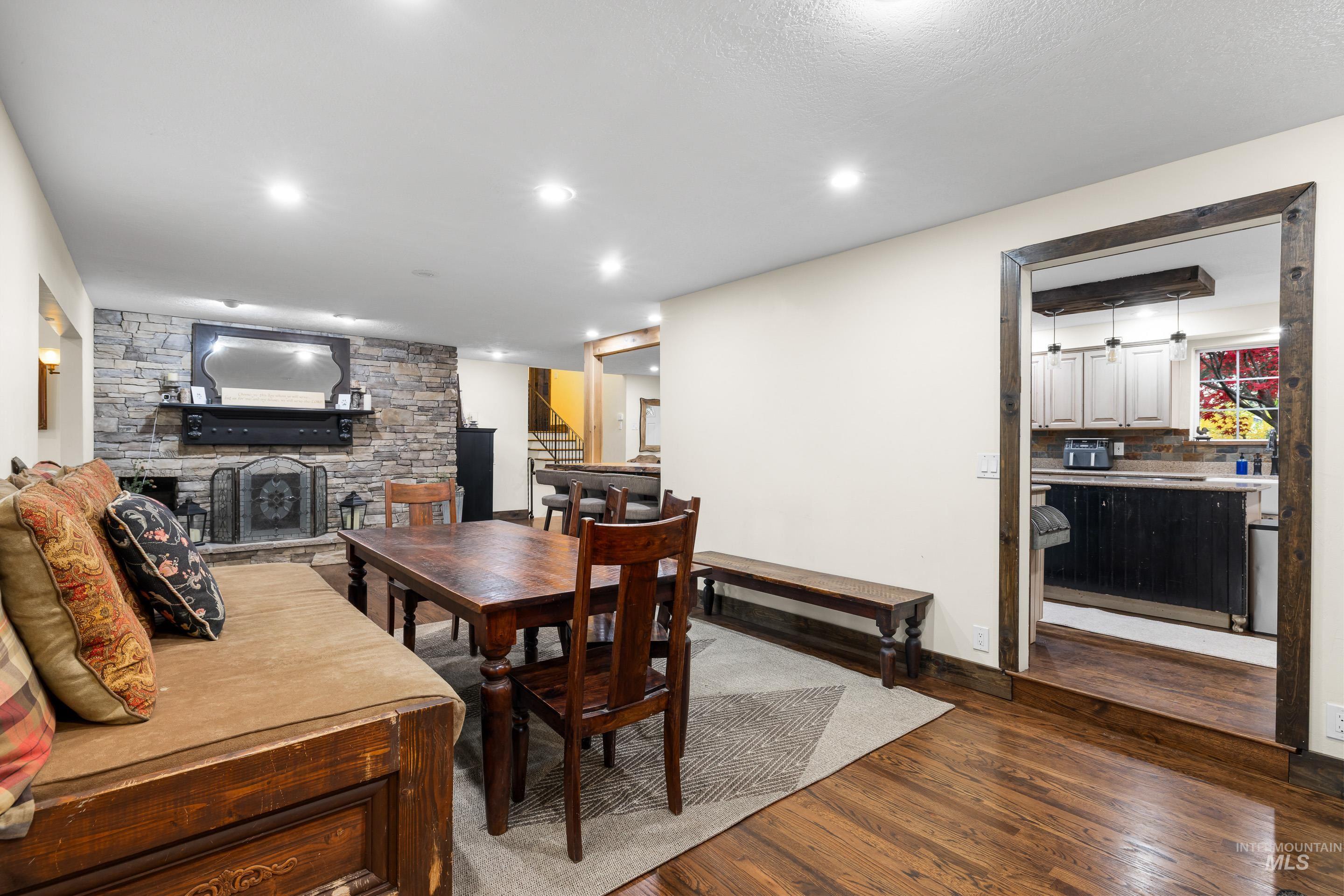 Dining area featuring dark wood-style flooring, a stone fireplace, stairs, and recessed lighting