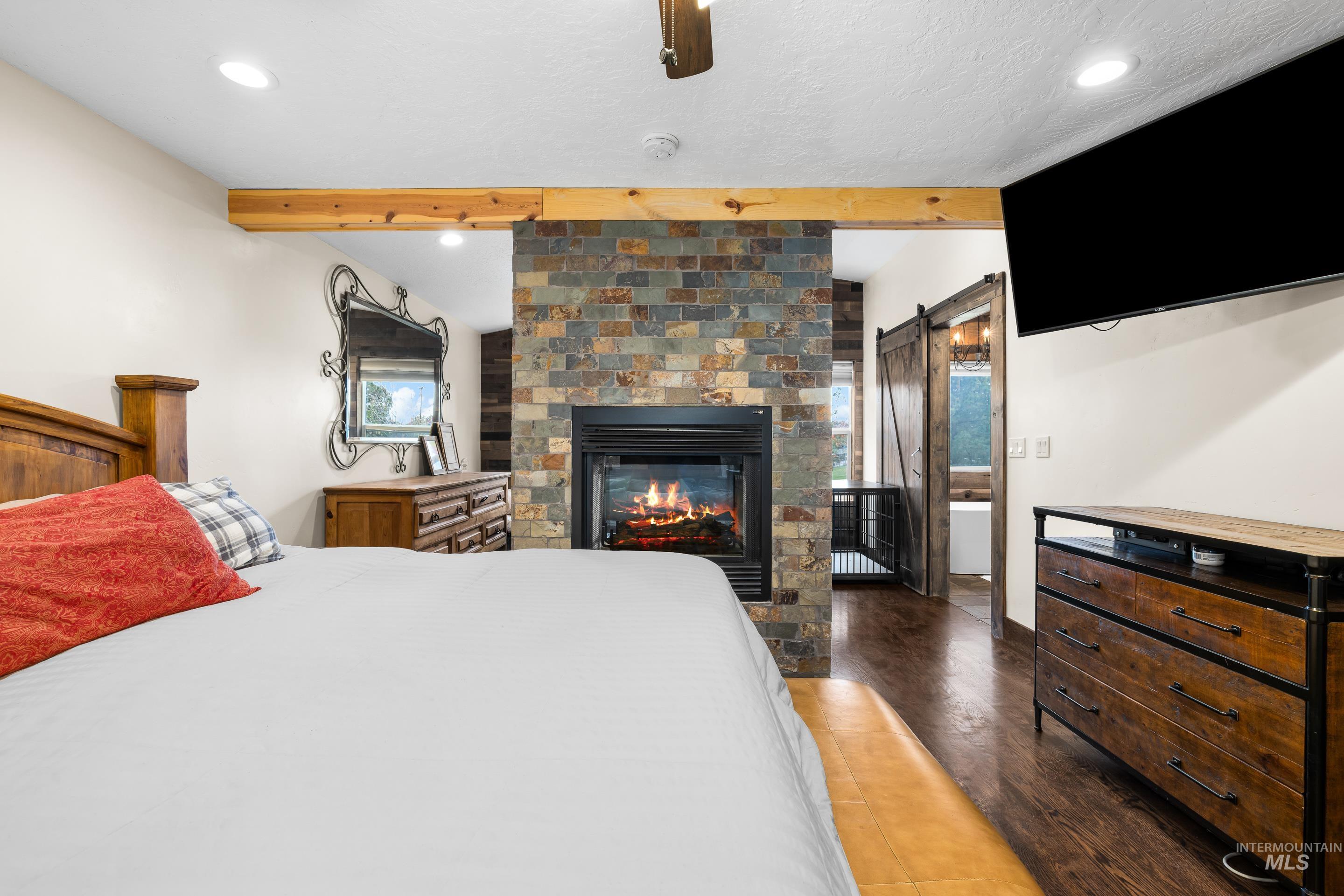 Bedroom featuring a barn door, wood finished floors, beam ceiling, a fireplace, and recessed lighting
