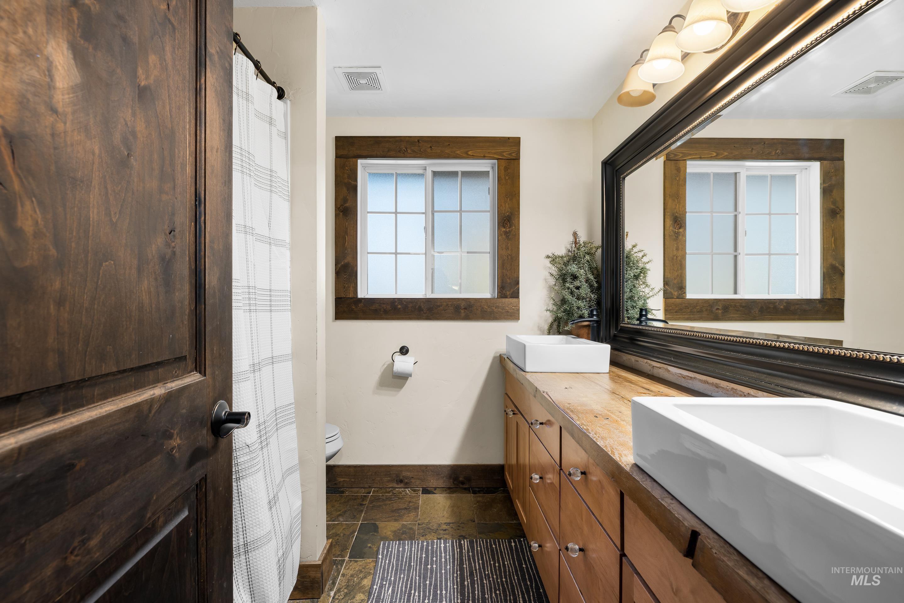 Full bath with double vanity, a shower with curtain, and stone tile flooring