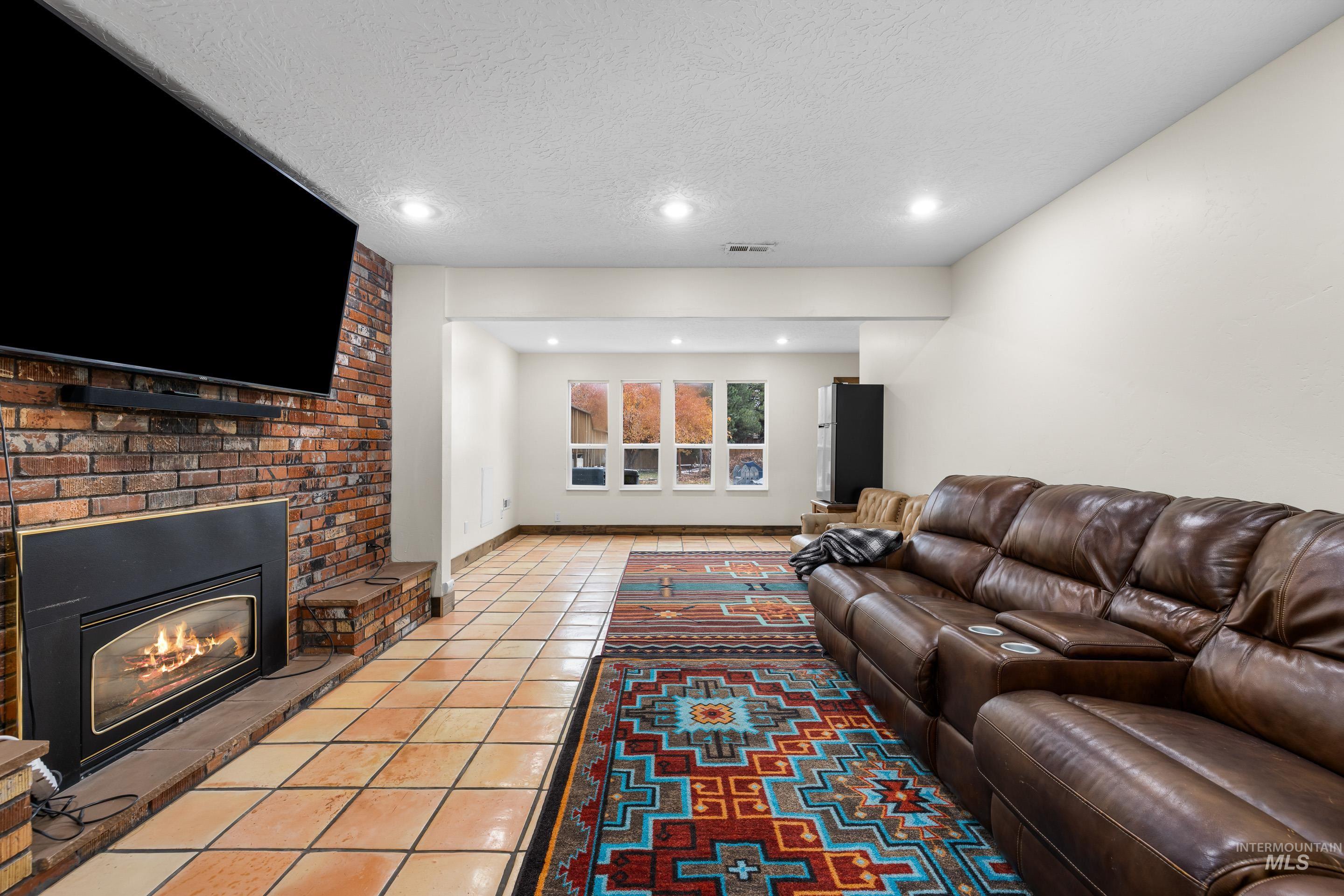 Living room featuring a textured ceiling, light tile patterned flooring, recessed lighting, and a brick fireplace
