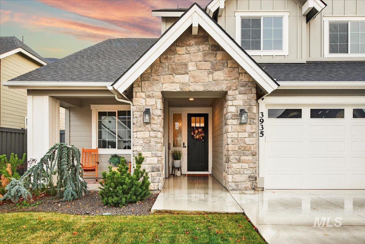 Exterior entry at dusk with board and batten siding, a shingled roof, and stone siding