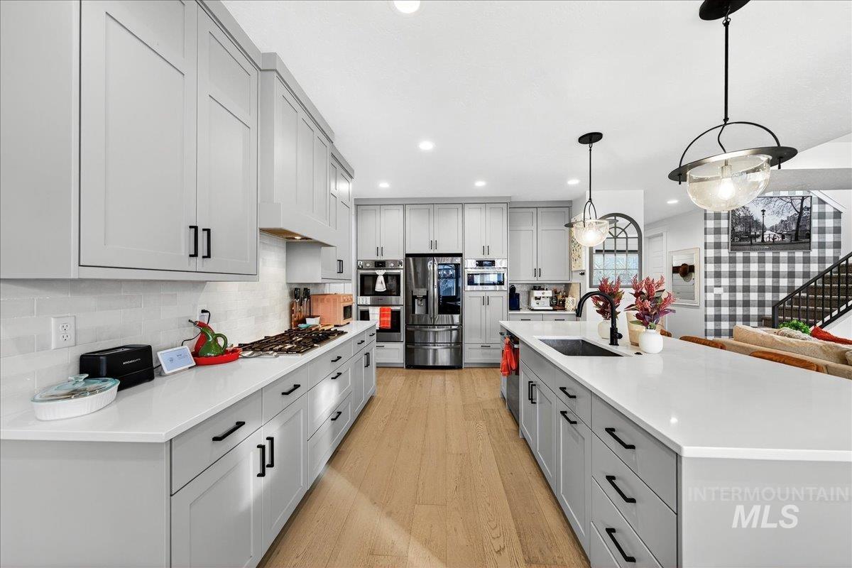 Kitchen with a spacious island, stainless steel appliances, gray cabinets, light wood finished floors, and decorative backsplash