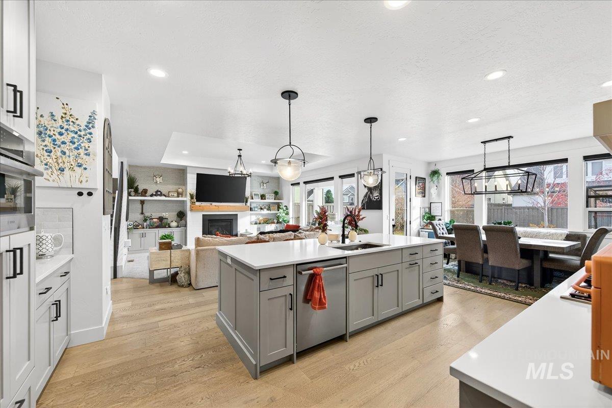 Kitchen featuring light wood-style flooring, a warm lit fireplace, hanging light fixtures, stainless steel appliances, and open floor plan
