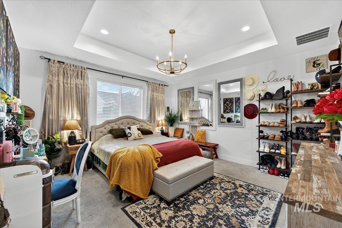 Carpeted bedroom with a tray ceiling, a chandelier, and recessed lighting