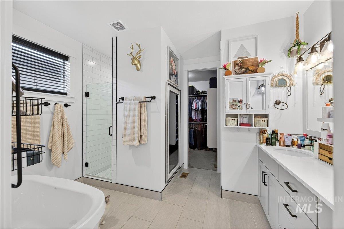 Bathroom with vanity, a spacious closet, a shower stall, a soaking tub, and light tile patterned flooring