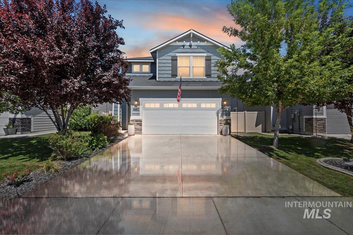 View of front of home with concrete driveway, an attached garage, stone siding, and a lawn