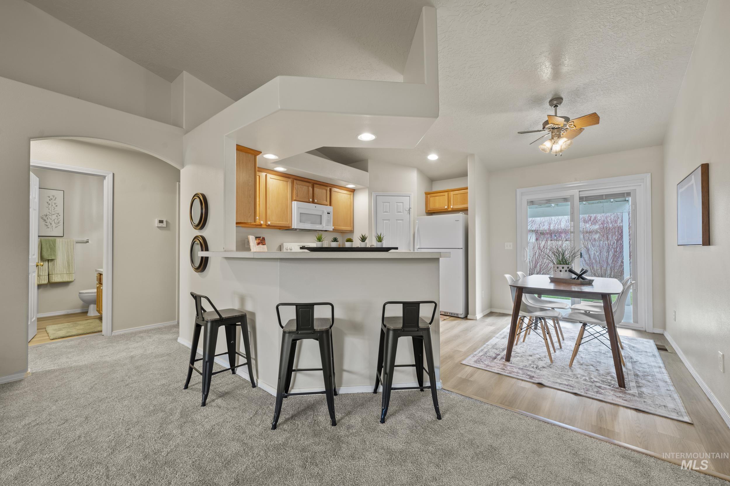 Kitchen featuring arched walkways, white appliances, recessed lighting, a kitchen breakfast bar, and a peninsula