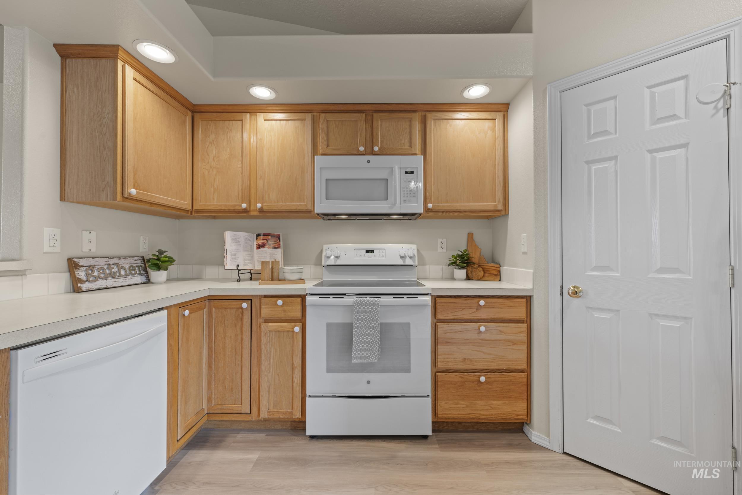 Kitchen with white appliances, light countertops, light wood-style floors, and recessed lighting