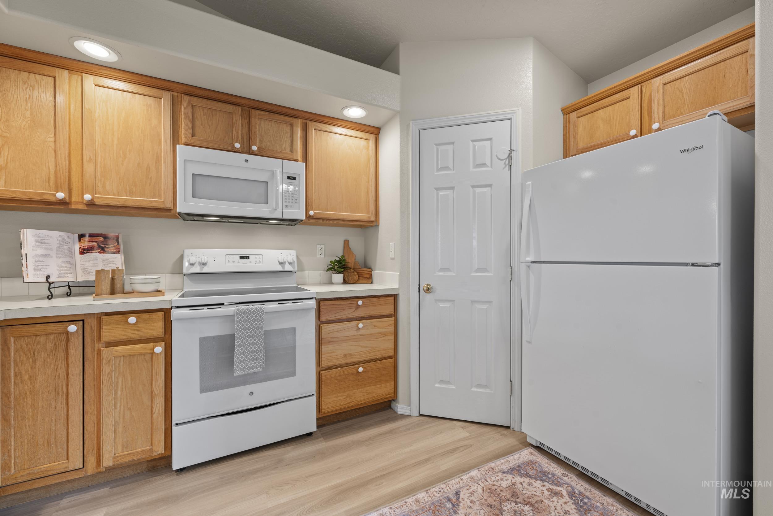 Kitchen featuring white appliances, light countertops, light wood-style flooring, and recessed lighting