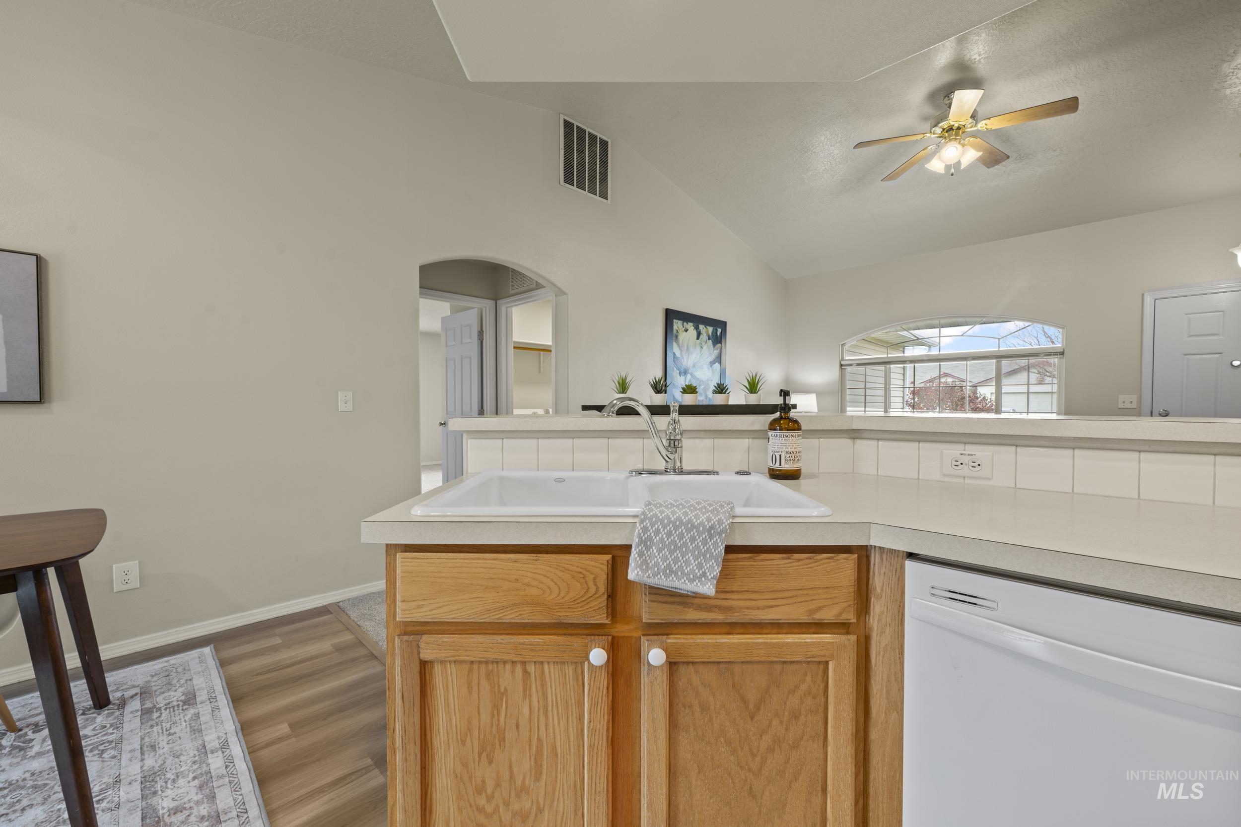Kitchen featuring white dishwasher, vaulted ceiling, light countertops, light wood-type flooring, and ceiling fan