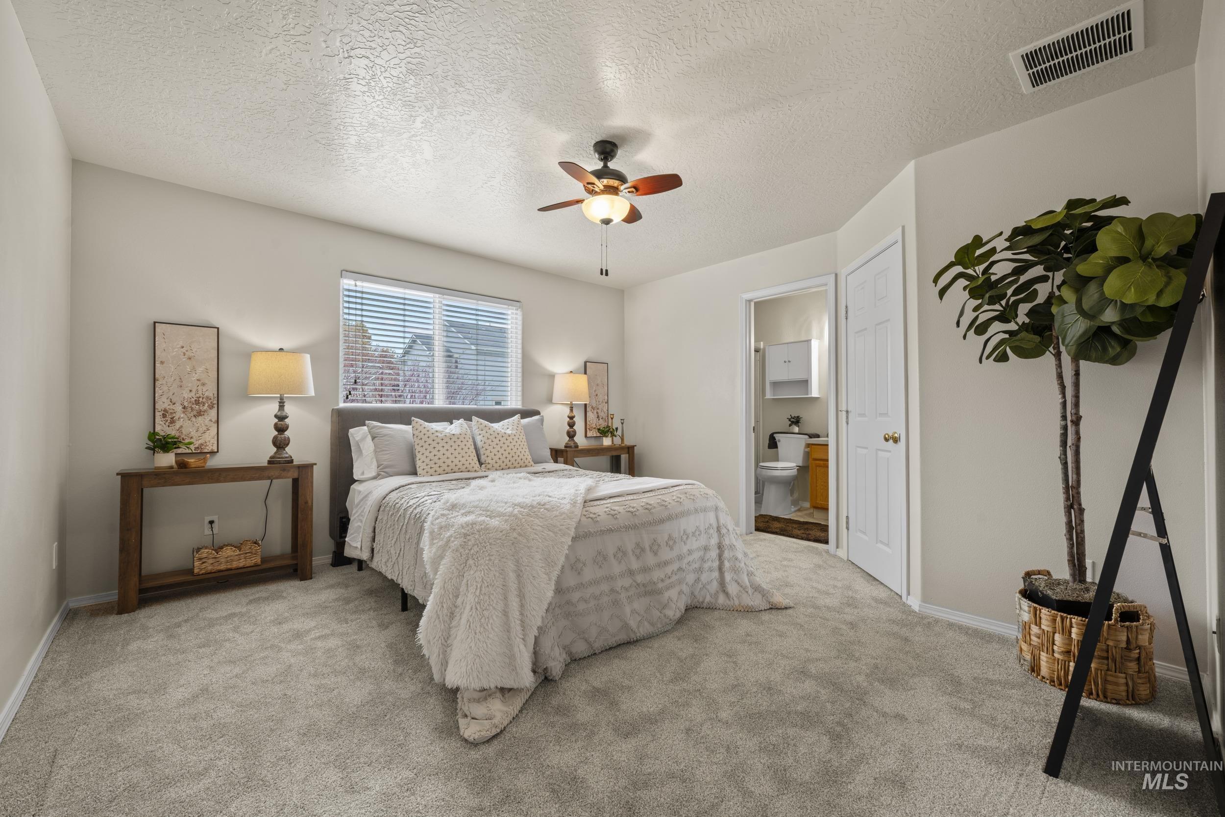 Carpeted bedroom with a textured ceiling, ceiling fan, and ensuite bathroom