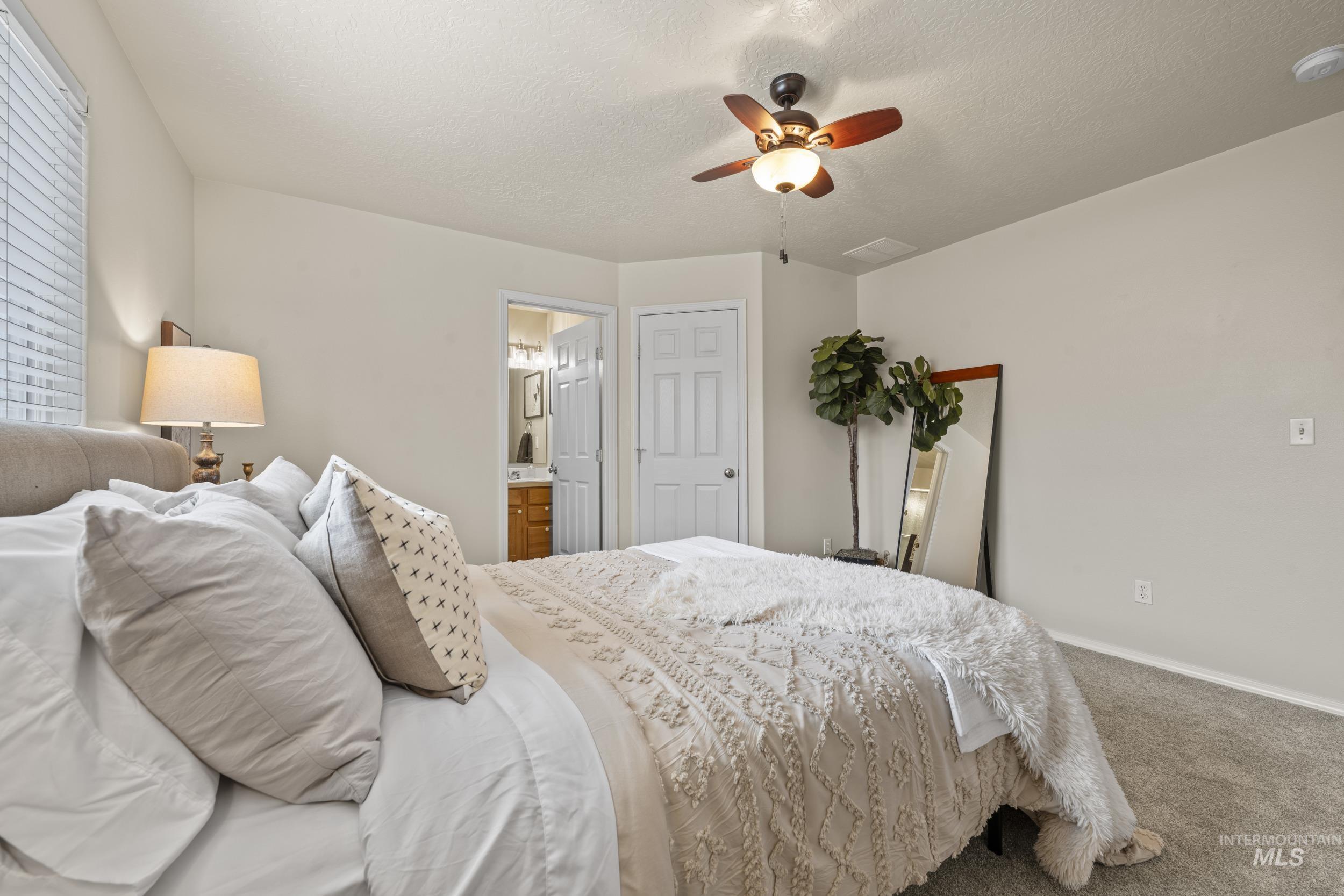 Carpeted bedroom with a textured ceiling, a ceiling fan, and ensuite bath