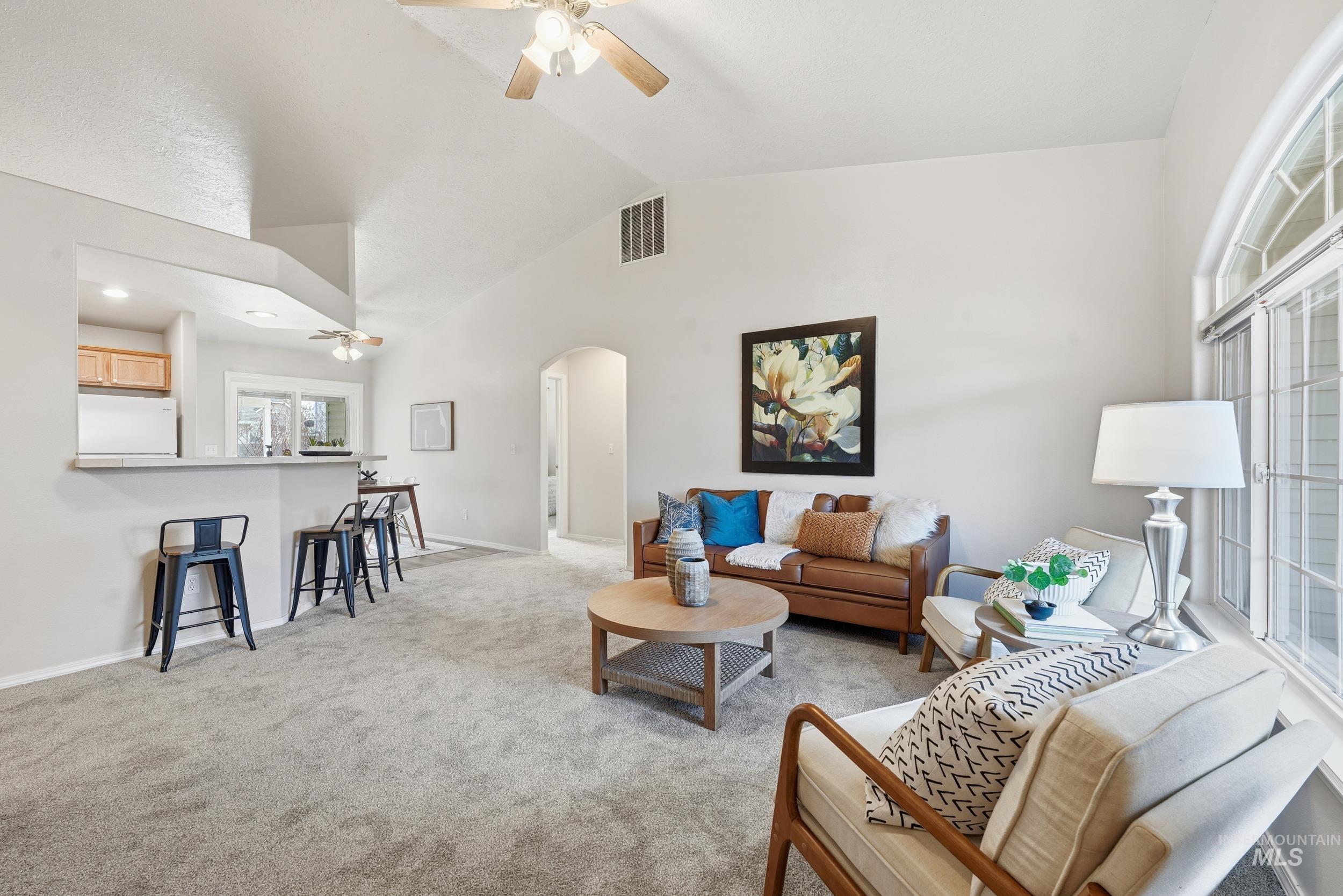 Living area featuring a ceiling fan, arched walkways, light carpet, and high vaulted ceiling