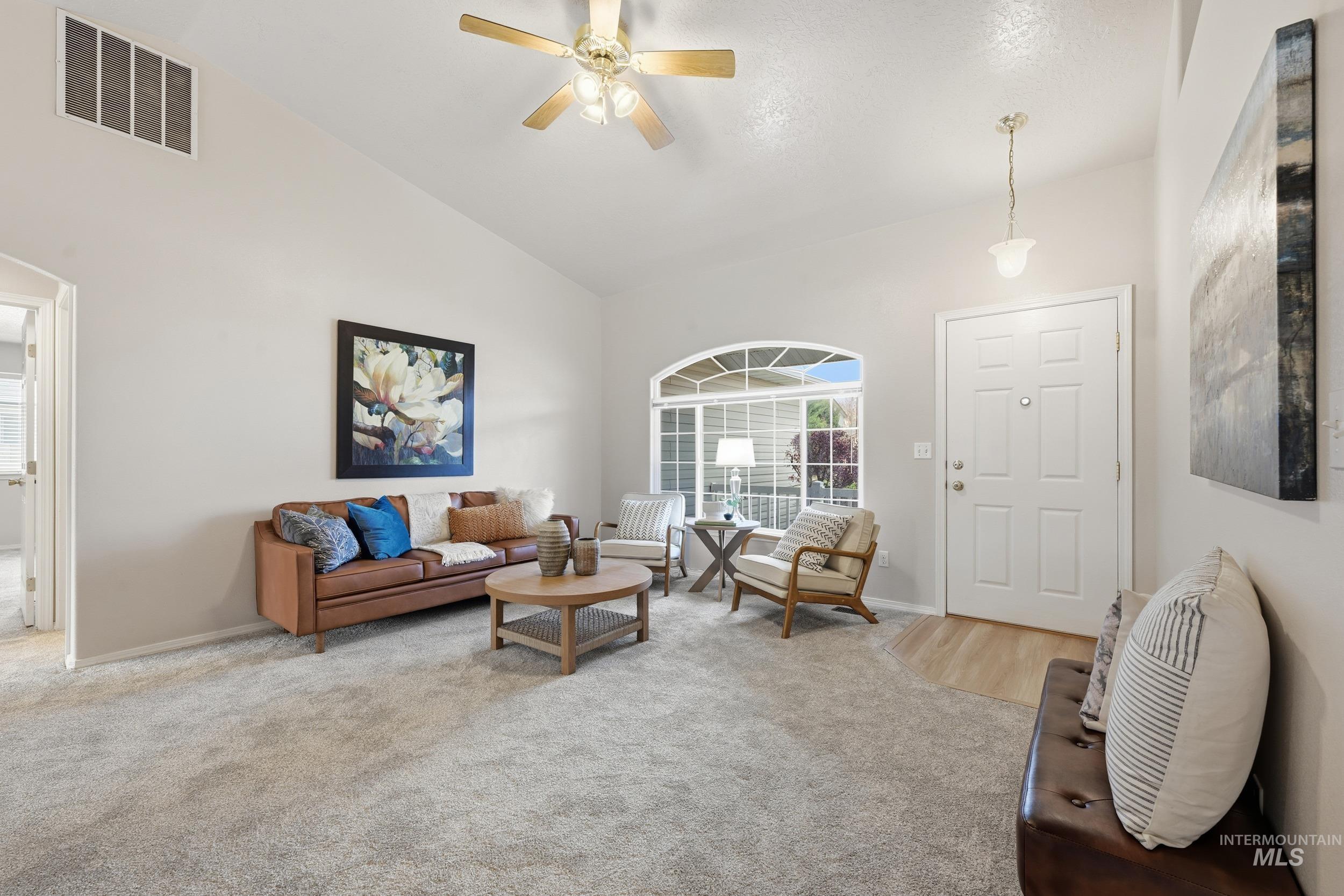Carpeted living room with a ceiling fan and high vaulted ceiling