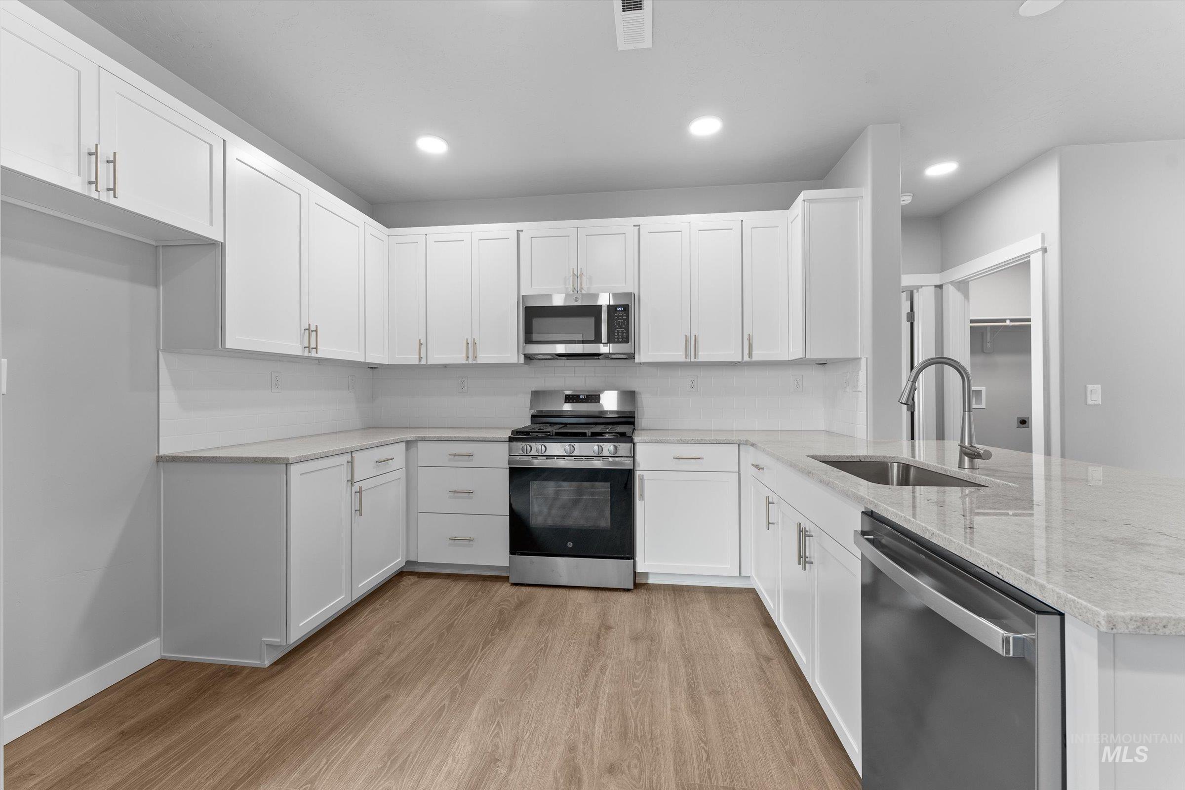 Kitchen with stainless steel appliances, light wood-style flooring, light stone counters, white cabinetry, and recessed lighting