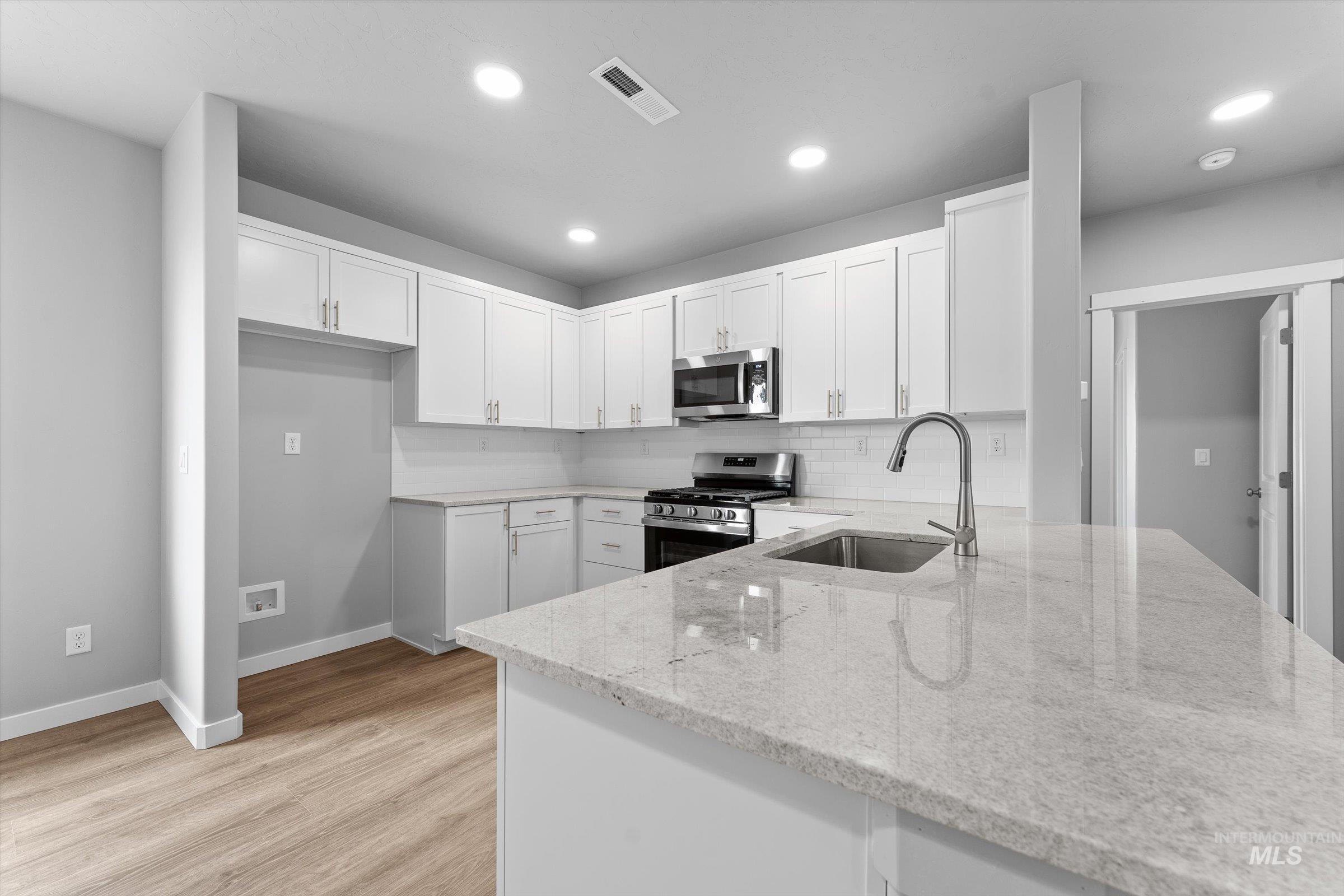 Kitchen with backsplash, white cabinets, appliances with stainless steel finishes, light wood-type flooring, and recessed lighting