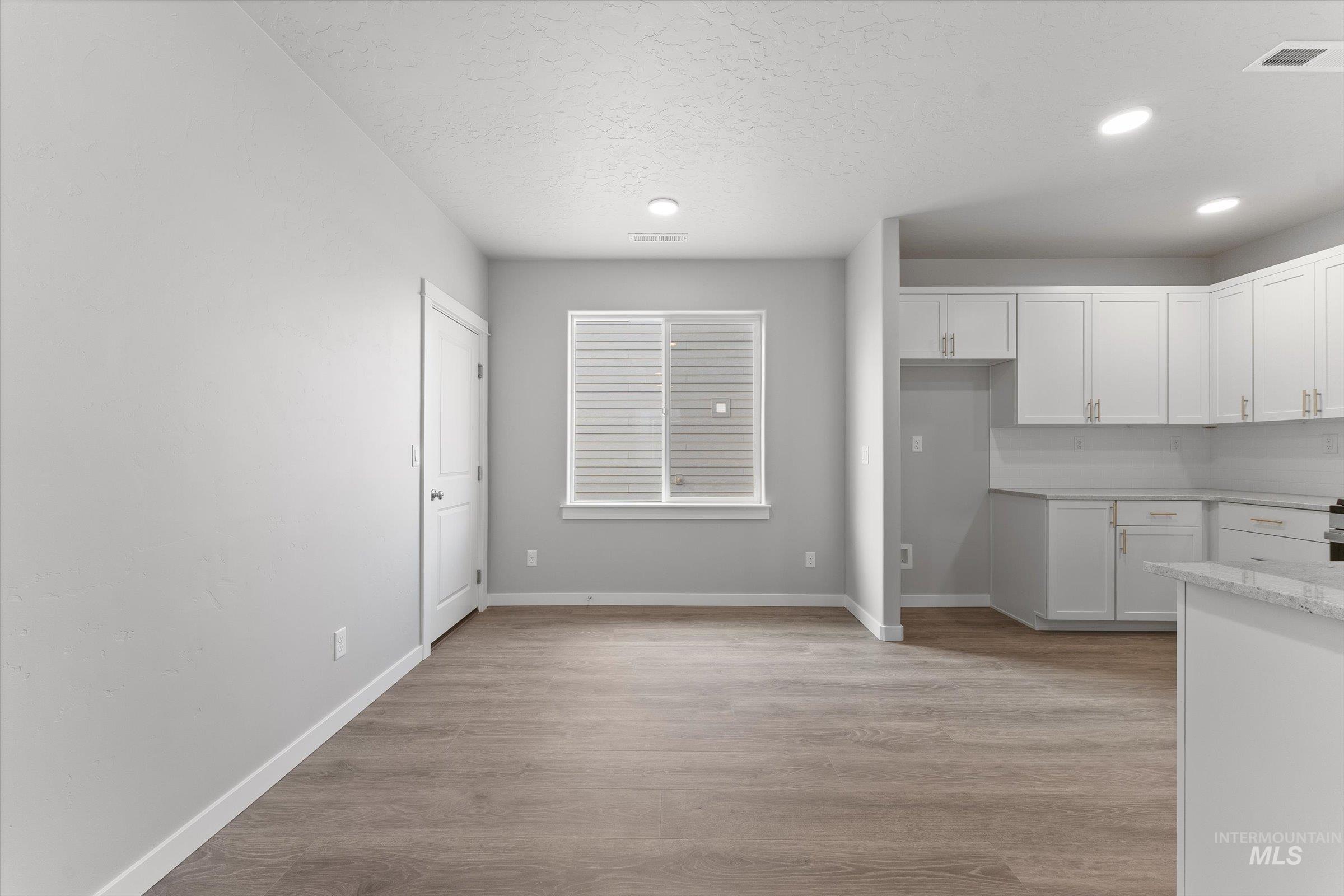 Kitchen with white cabinetry, light wood finished floors, light stone countertops, recessed lighting, and a textured ceiling