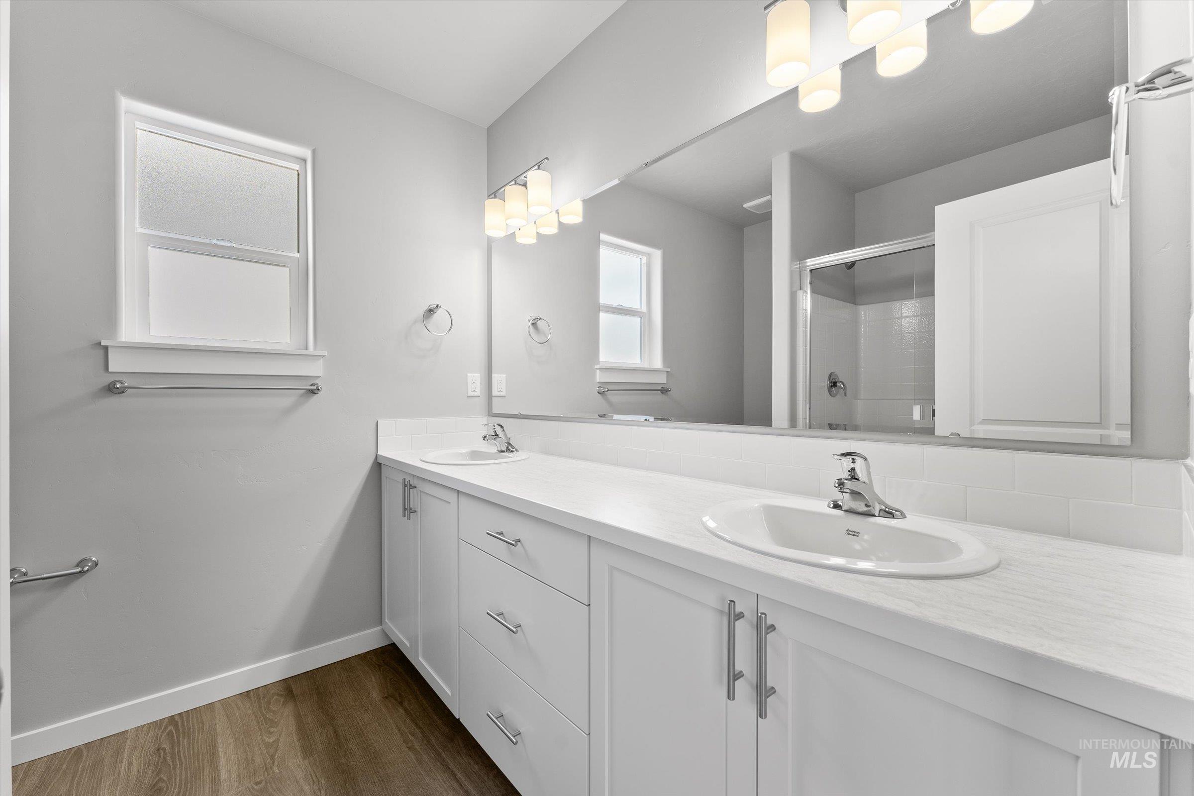 Full bathroom featuring double vanity, dark wood-style flooring, and a shower stall