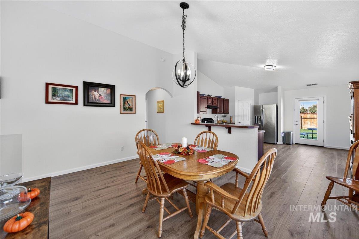 Dining room featuring arched walkways, vaulted ceiling, dark wood-type flooring, a chandelier, and a textured ceiling