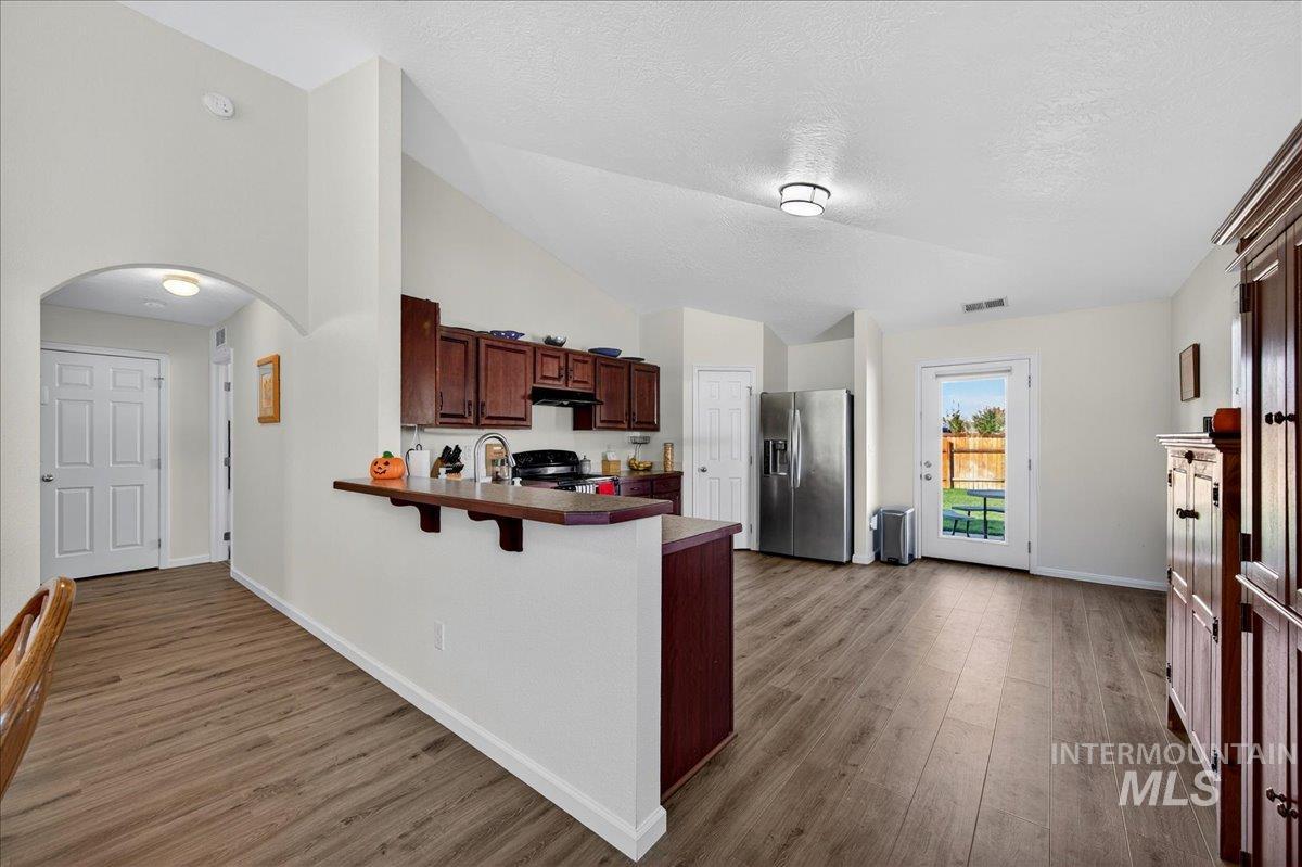 Kitchen with arched walkways, stainless steel fridge with ice dispenser, dark wood-type flooring, a peninsula, and a textured ceiling
