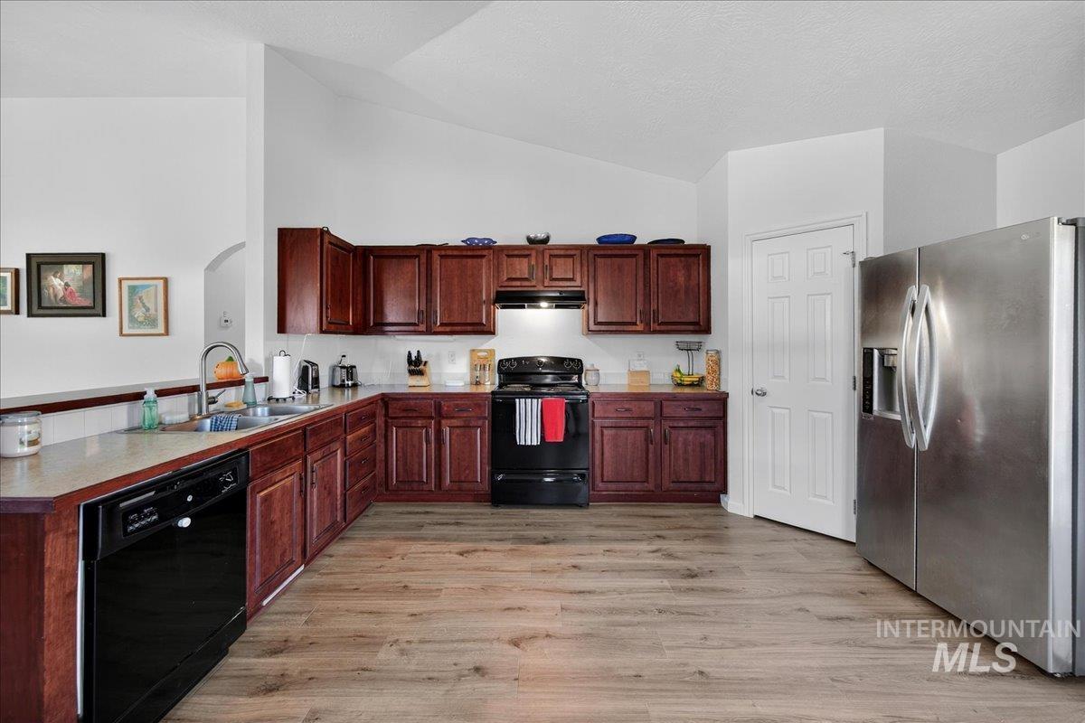 Kitchen with black appliances, light wood-style floors, light countertops, a peninsula, and under cabinet range hood