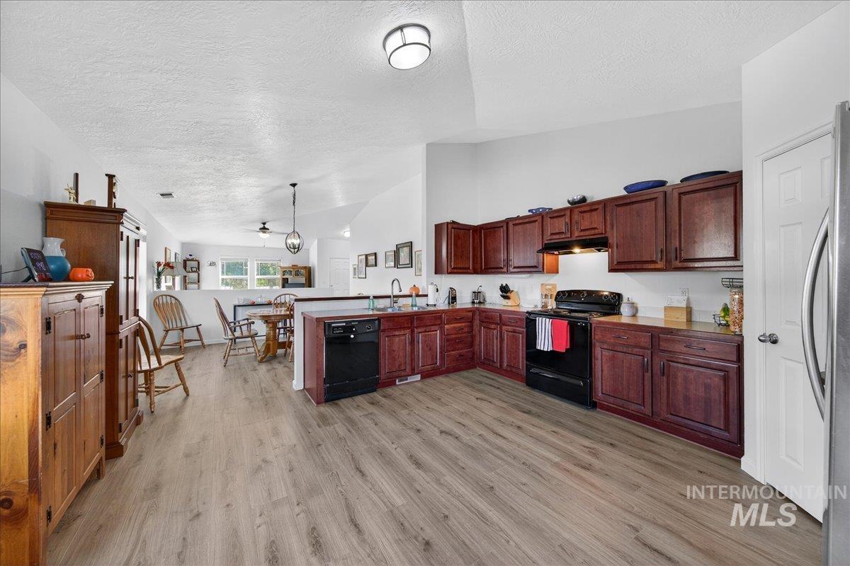 Kitchen with vaulted ceiling, a peninsula, a textured ceiling, black appliances, and light wood-style flooring