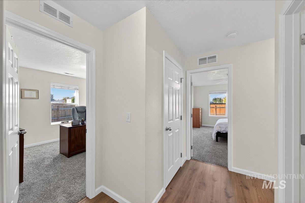 Hall featuring wood finished floors, a textured ceiling, a desk, carpet flooring, and a textured wall