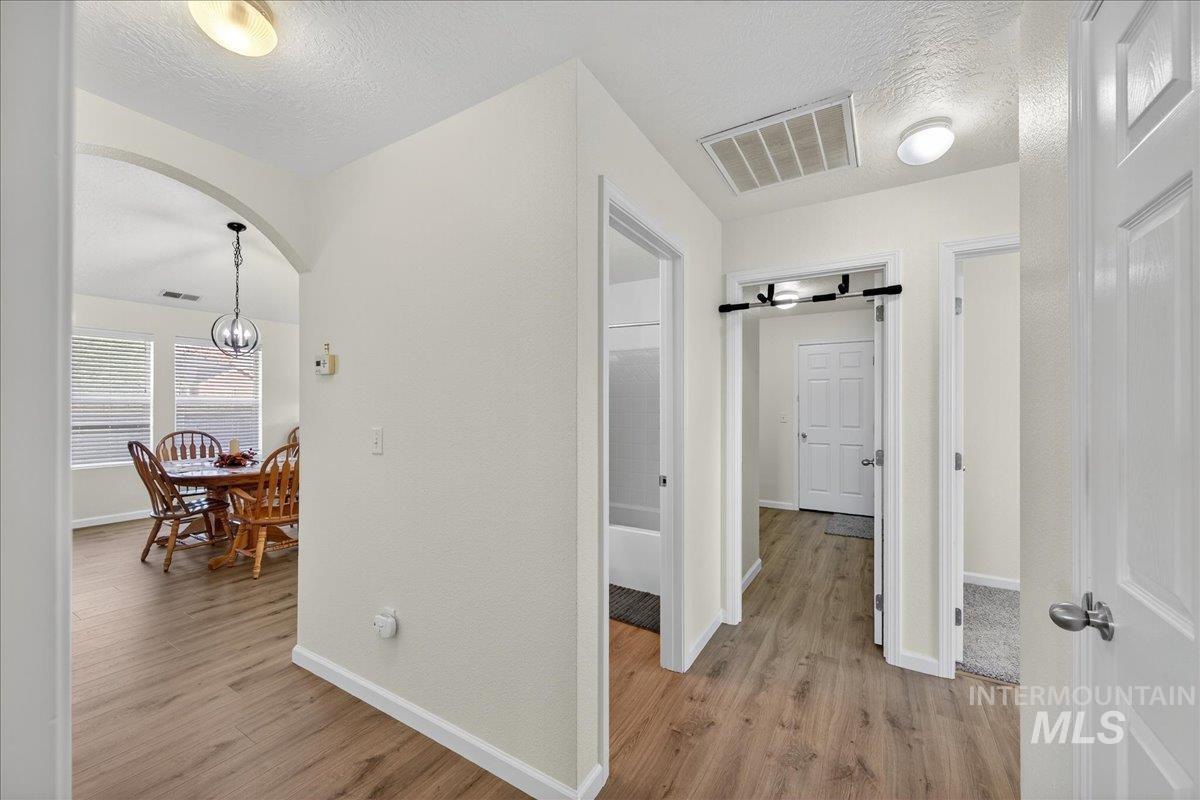 Hallway with a textured ceiling, light wood-style flooring, and arched walkways